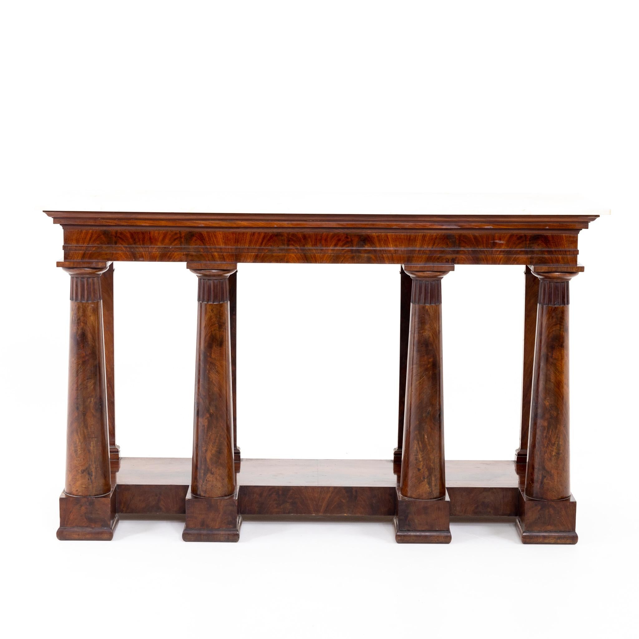 Large console veneered in mahogany with a light-colored marble top and an architecturally structured lower section, each with four columns and pilasters.