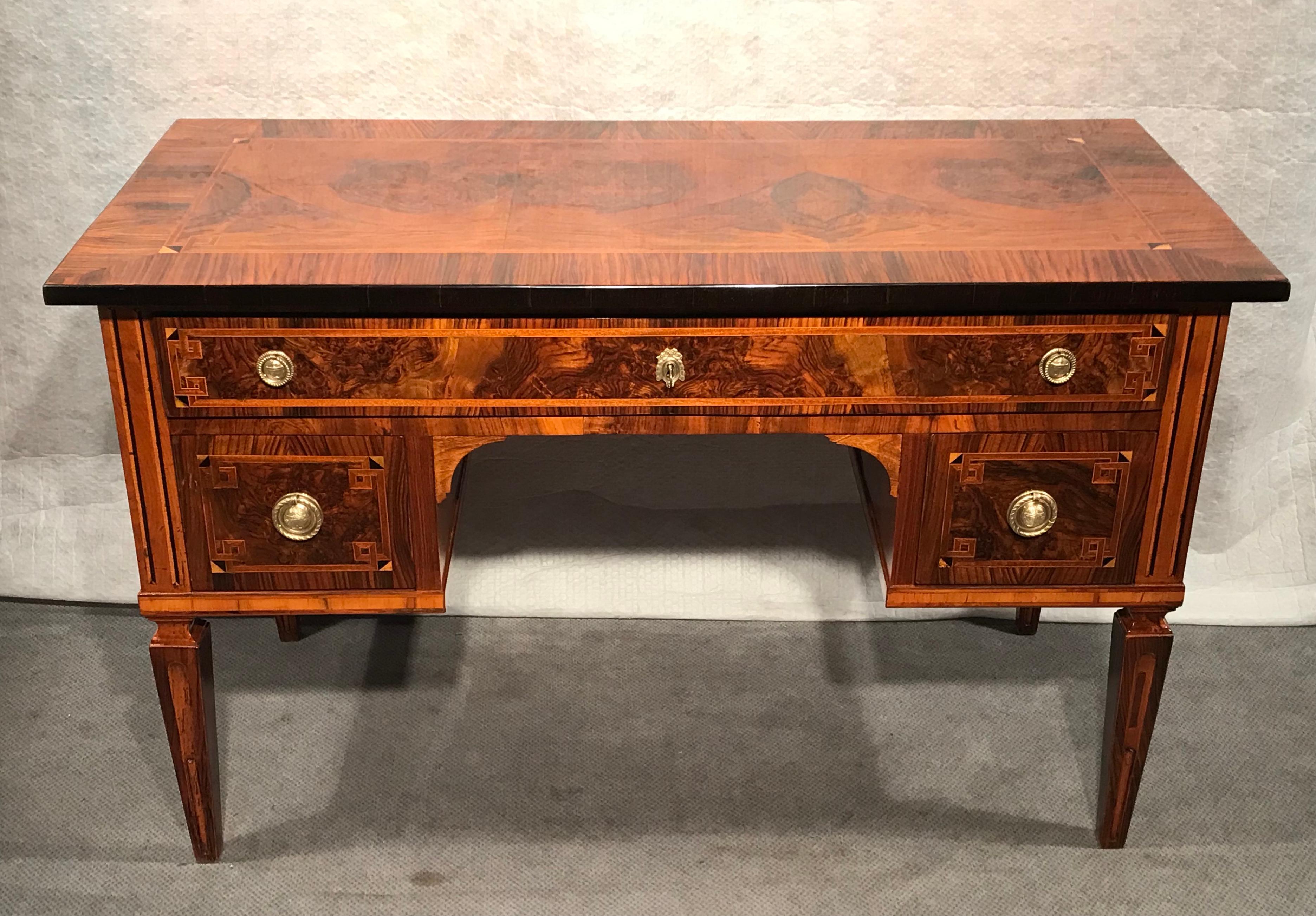 Dieser originale Louis XVI-Schreibtisch zeichnet sich durch sein schönes Nussbaumfurnier aus, das zusätzlich mit Intarsien verziert ist. Der Schreibtisch steht auf vier spitz zulaufenden Vierkantbeinen. Er hat drei Schubladen. Die Platte hat ein