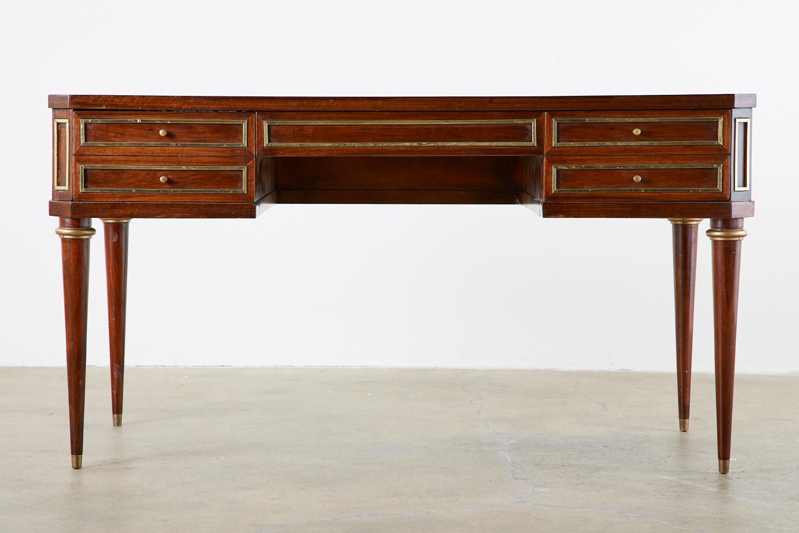 Distinctive mahogany writing table or desk featuring a case embellished with brass panel accents and fronted by three large storage drawers. The case is rectangular with angular clipped corners and supported by bronze mounted round tapered legs