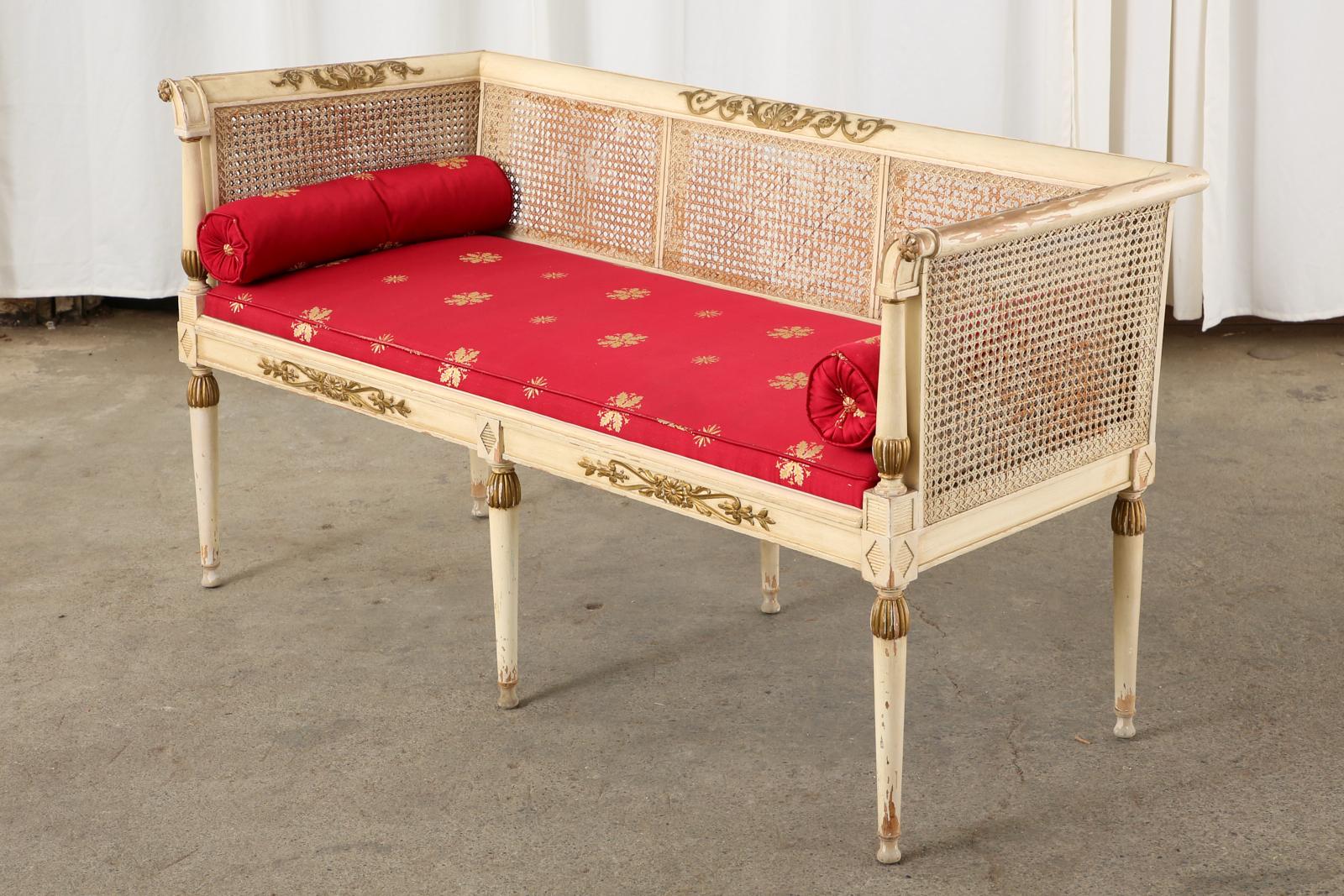 Fantastic Mid-Century Modern Italian painted settee or bench seat featuring caned sides and seat. Crafted in the neoclassical Directoire taste of late 18th century France. The lacquered frame is decorated with rosettes and rocaille in a parcel gilt