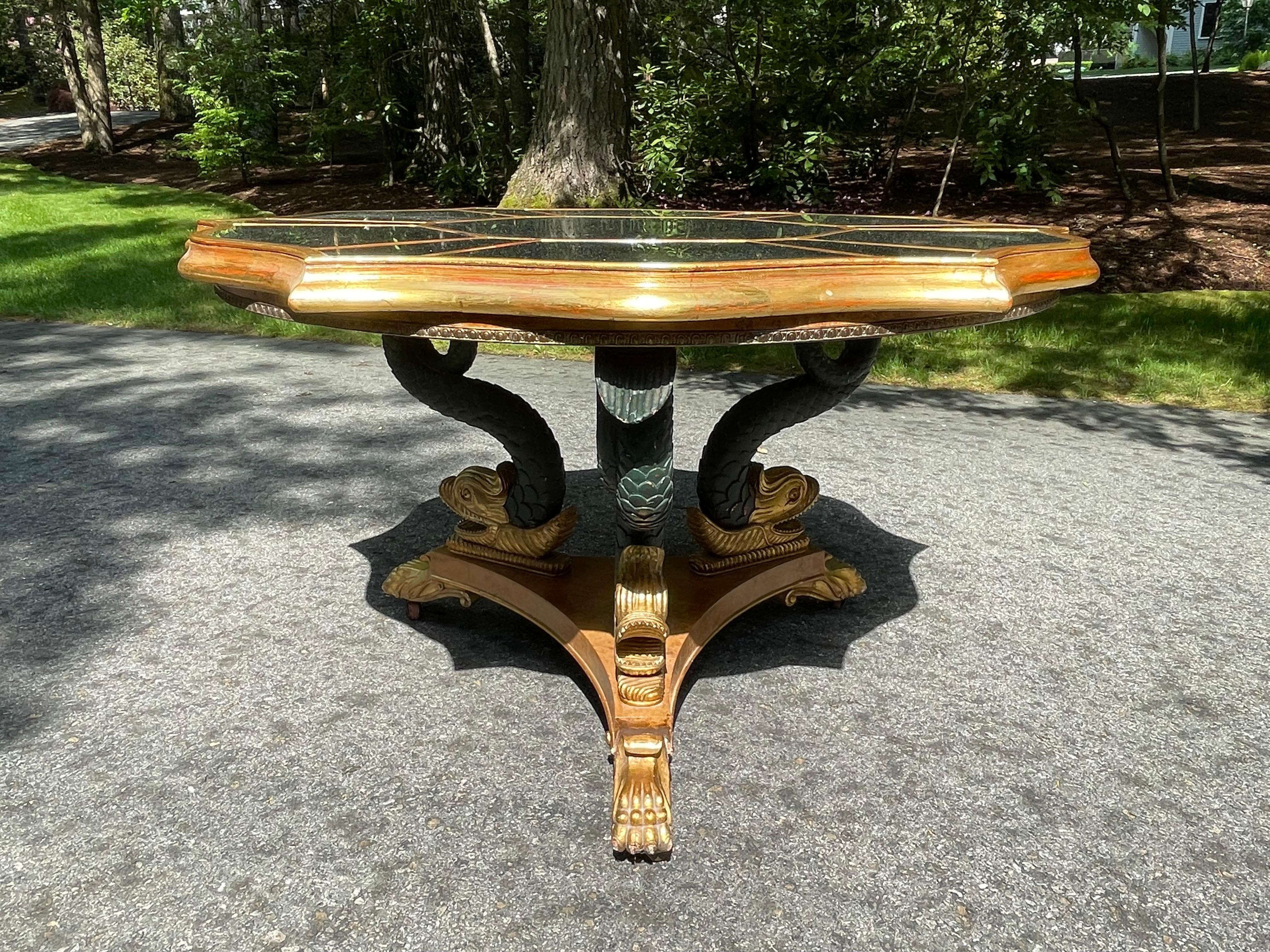Three beautifully hand carved dolphins rest on a three sided burr Walnut inlaid platform. Their tails support an antique mirrored six sided scalloped top guided in 24k gold.
The design is after English architect and furniture designer William Kent.