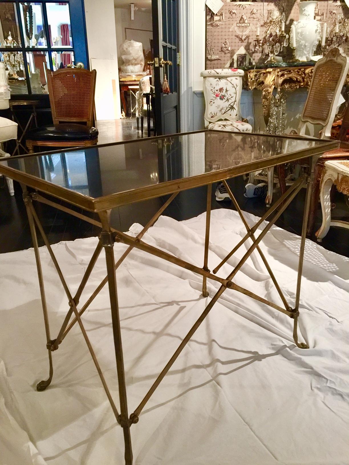 A Classic neoclassical French Empire style bronze and black marble rectangular guéridon table on slender bronze legs with paw feet. The rectangular black marble-top is surrounded by a decorative bronze band. The legs are joined by an openwork
