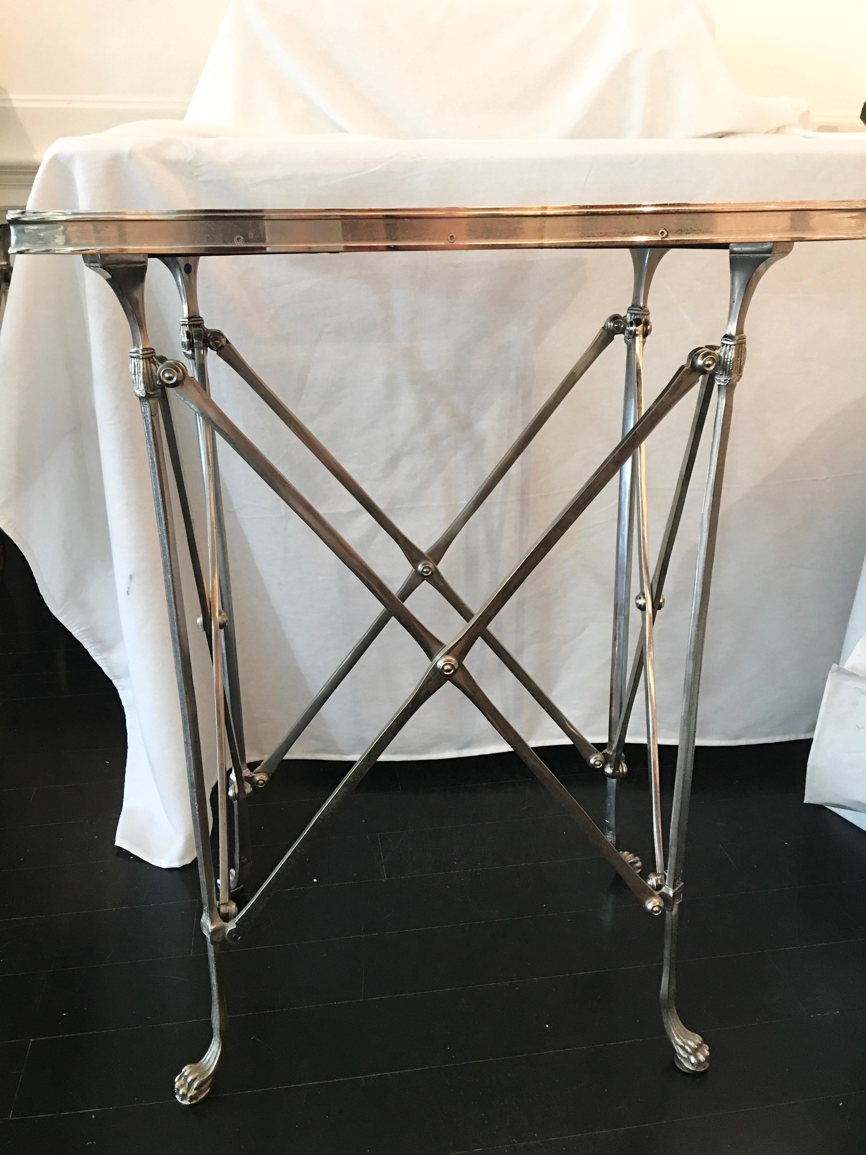 A classic neoclassical French Empire style nickeled Gueridon table with mirror top is supported by slender bronze legs with paw feet. The rectangular mirror top is surrounded by a decorative bronze band. The legs are joined by an openwork triangular