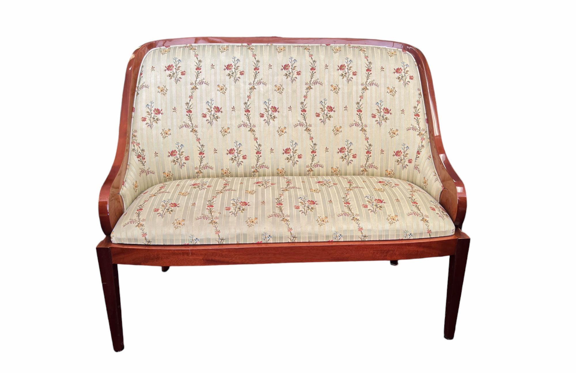 Presenting a magnificent English art deco pair of benches/loveseats, custom handcrafted, featuring flame mahogany veneer in a high gloss finish. The benches are upholstered in a subtly striped pale green textile with a delicate floral pattern. The