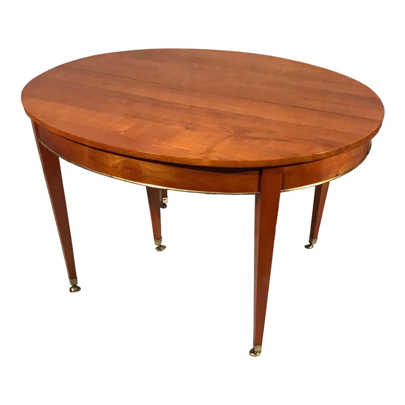 This elegant Neoclassical Dining Room Table dates back to the mid 19th century and comes from Germany. The table features a pretty cherry veneer and has a brass band around the apron. It stands on six tapered legs with their original brass casters.