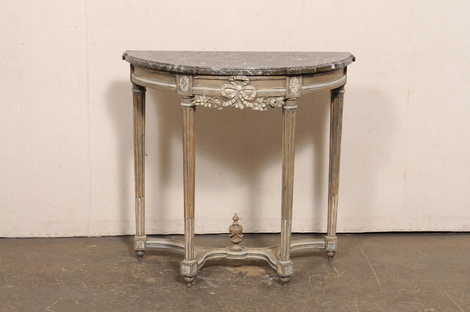 A French Neoclassical nicely-carved demi lune console table, with its original marble top and carved urn finial accent at underside, from the 19th century. This antique table from France features a half-circular/demi shaped marble top, which rests