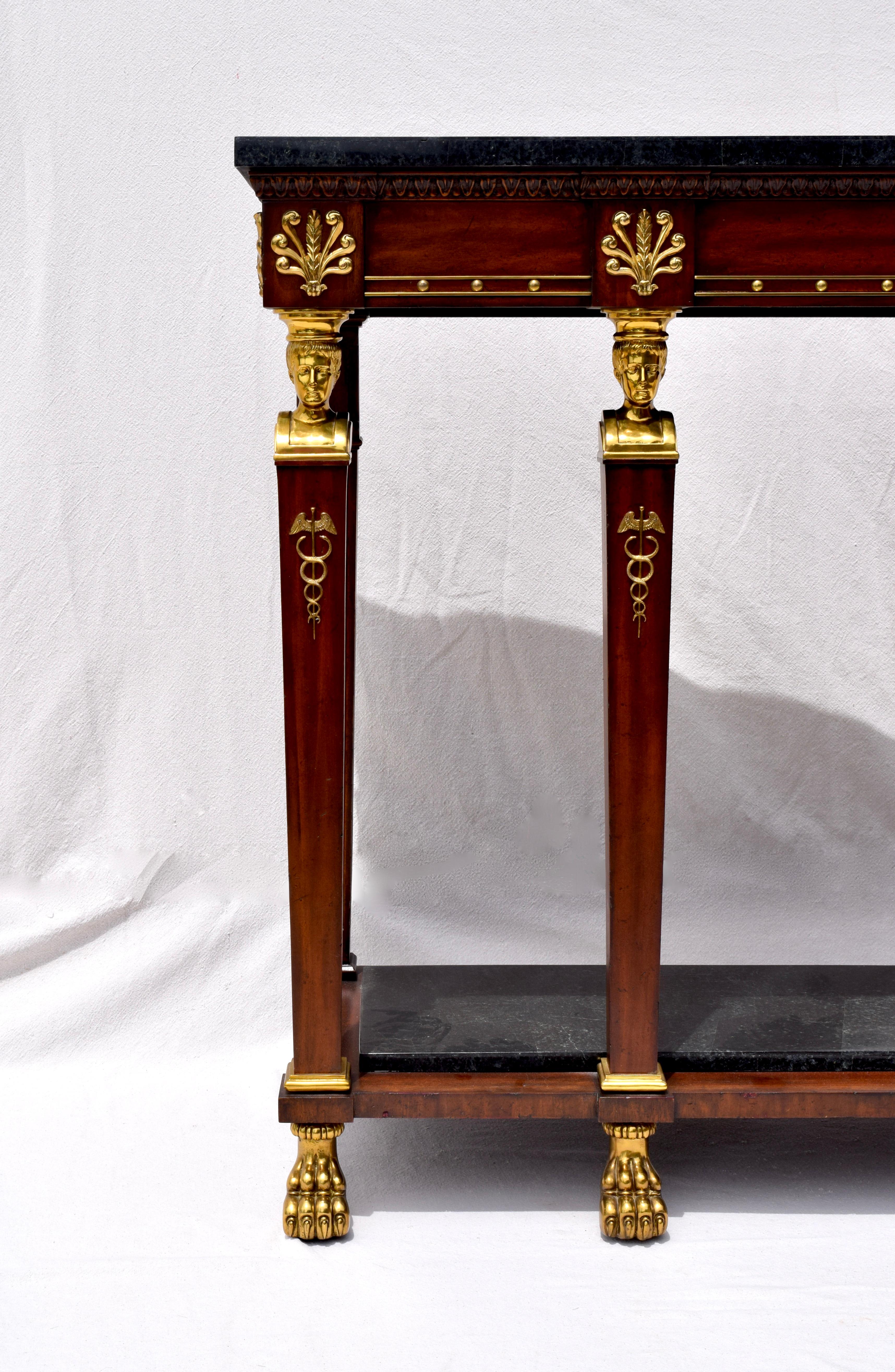 A stately Maitland Smith two tier mahogany and brass Pier table. Neoclassical in style having stationary tessellated black marble top and base with ornate brass design elements throughout and carved frieze.