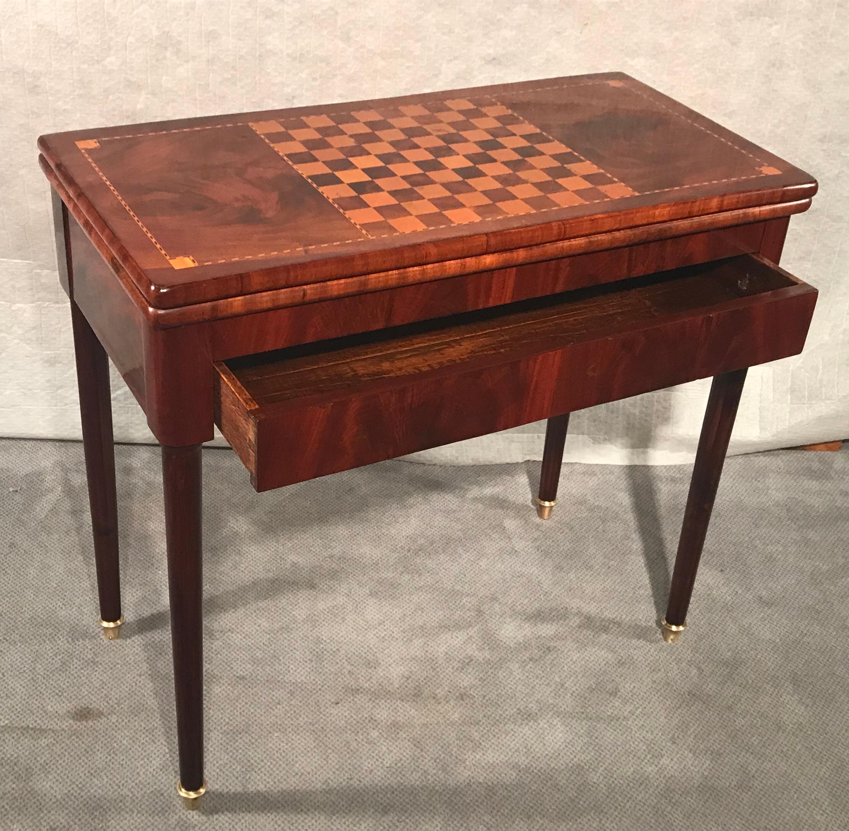 Cette table de jeu néoclassique de France date de 1810-20. Il comporte un échiquier sur le dessus qui est encadré par un élégant ruban incrusté. L'intérieur de la table est décoré d'un feutre vert. Le plateau déplié peut être tourné et repose alors