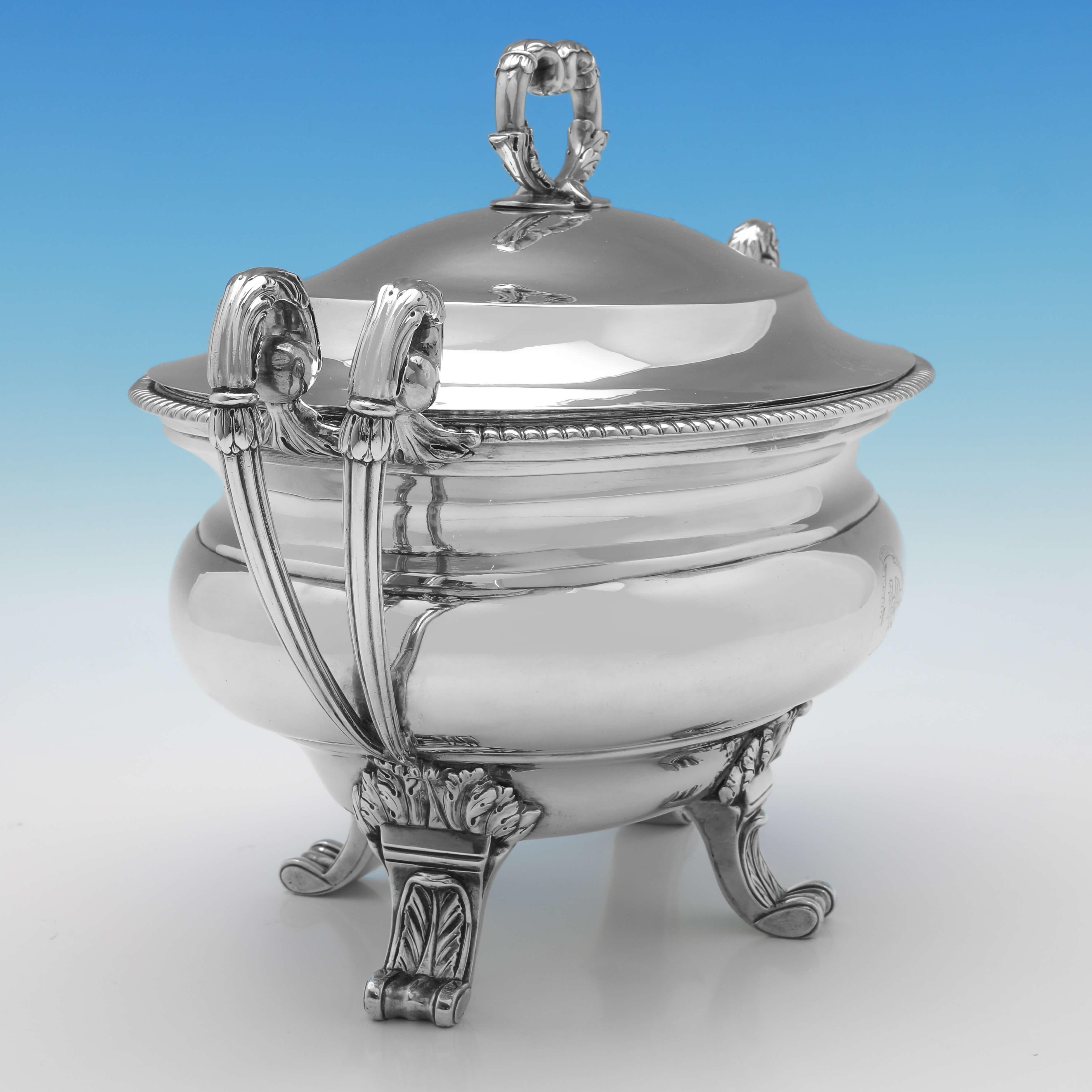 Hallmarked in London in 1799 by William Pitts, this stylish, George III, Antique Sterling Silver Soup Tureen, features unusual double scroll handles, four acanthus detailed feet, an engraved crest and motto, and a gadroon border. 

The soup tureen