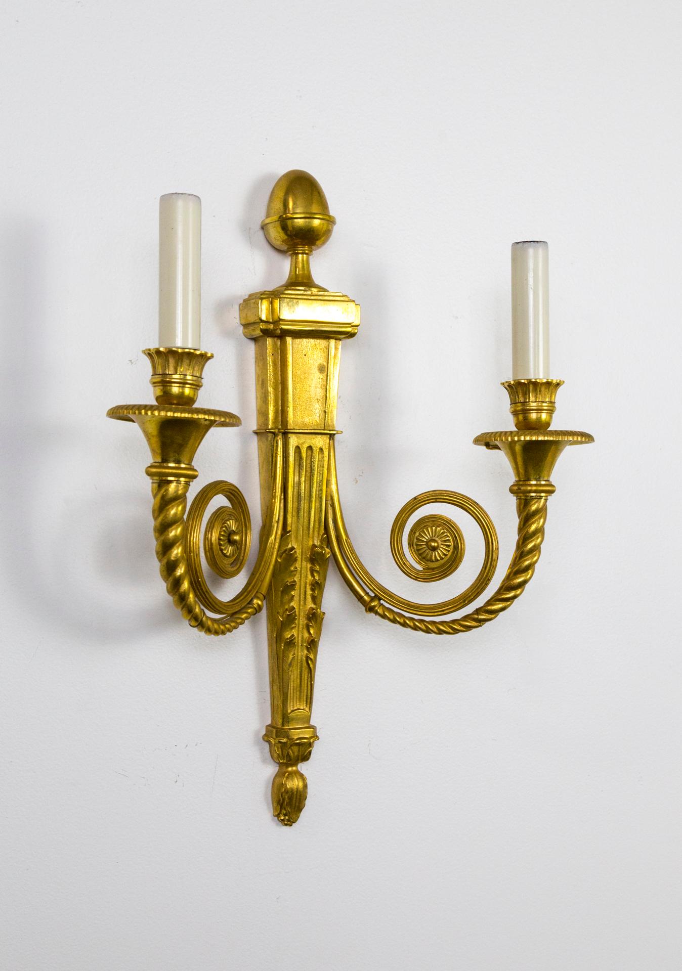 A gorgeously proportioned pair of neoclassical, gilded bronze 2-arm sconces; with acanthus leaf, acorn, swirl, and rosette detailing. Late Belle Époque style, France. Early 1900s. Measures: 18” height x 14” width x 5” depth. Two pair available.