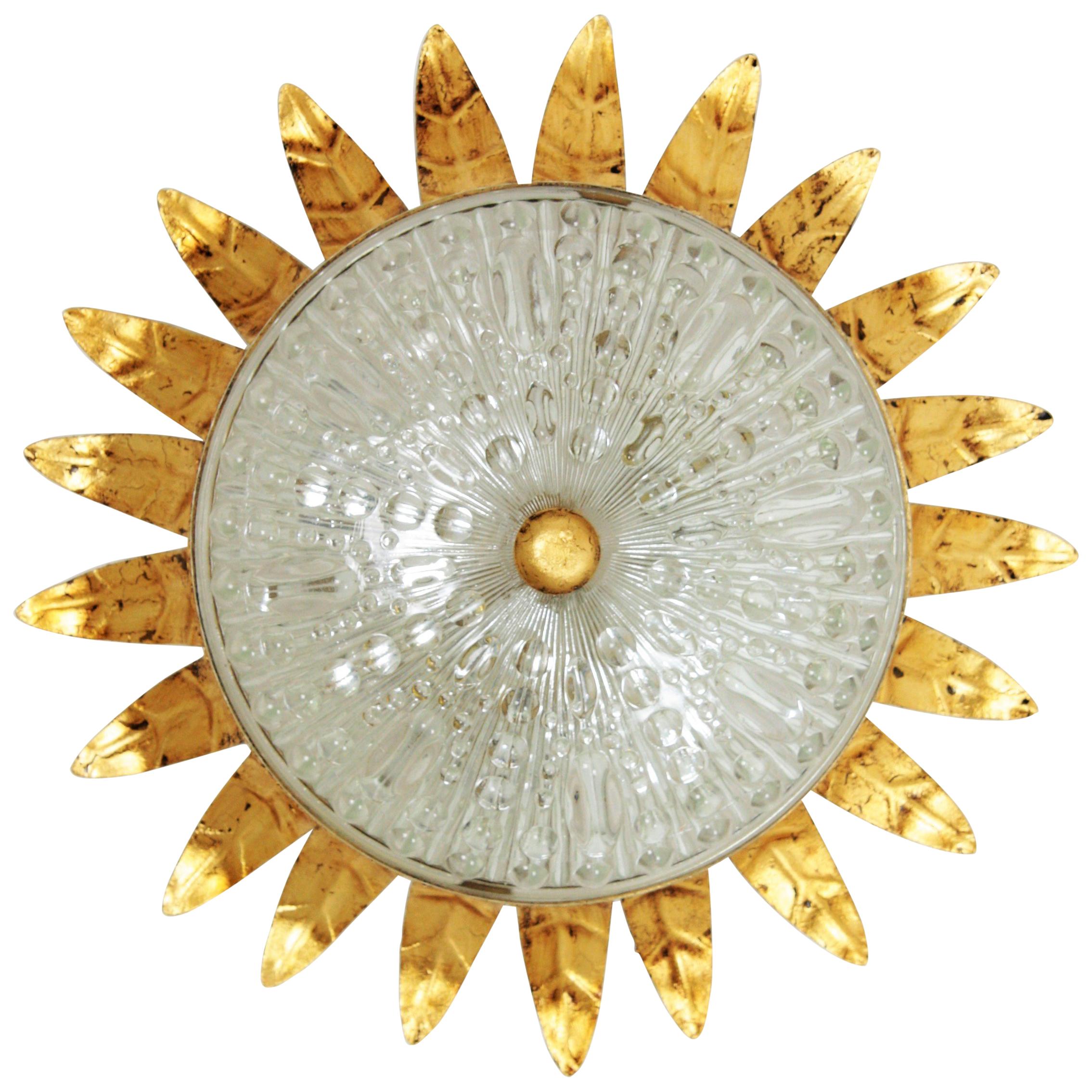 An sculptural hand-hammered iron and glass sunburst ceiling light fixture in neoclassical style, Spain, 1940-1950.
A hand-hammered gilt iron sunburst crown fixture with a pressed glass shade with a gilt iron ball finial.
This flush mount has a