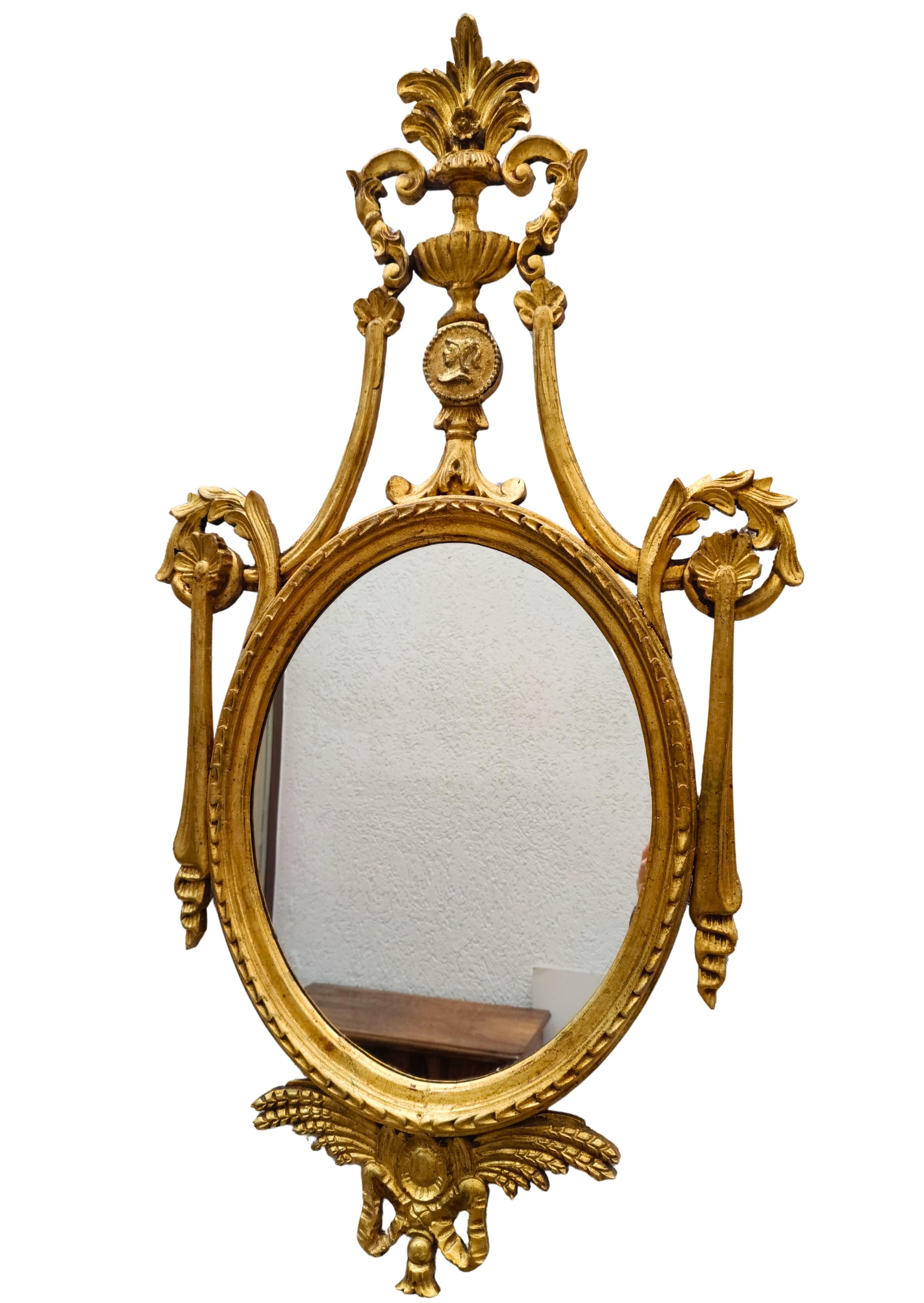 This original neoclassical wall mirror was crafted in Southern Germany around 1800. The oval frame is made of spruce wood with finely modelled gesso ornaments and richly carved details. The upper section is crowned by a classical urn with acanthus