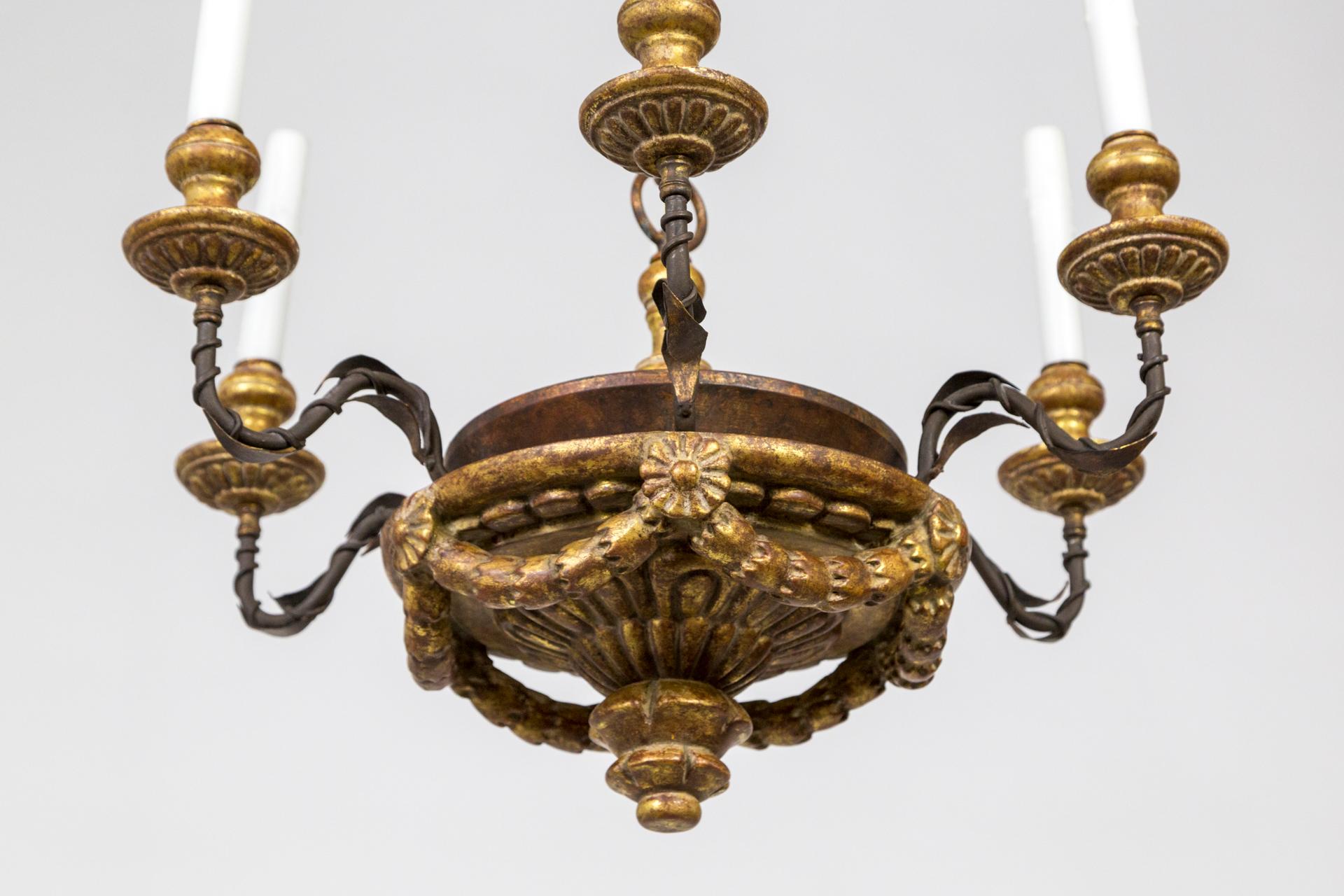 A neoclassical, 6-arm candlestick chandelier by Dennis & Leen.  It has a carved wood, bowl-shaped body, and S-curve black iron arms with vines spiraling around them.  It is gilt with 22k gold on the candle cups, rosette garlands, and finial.  With