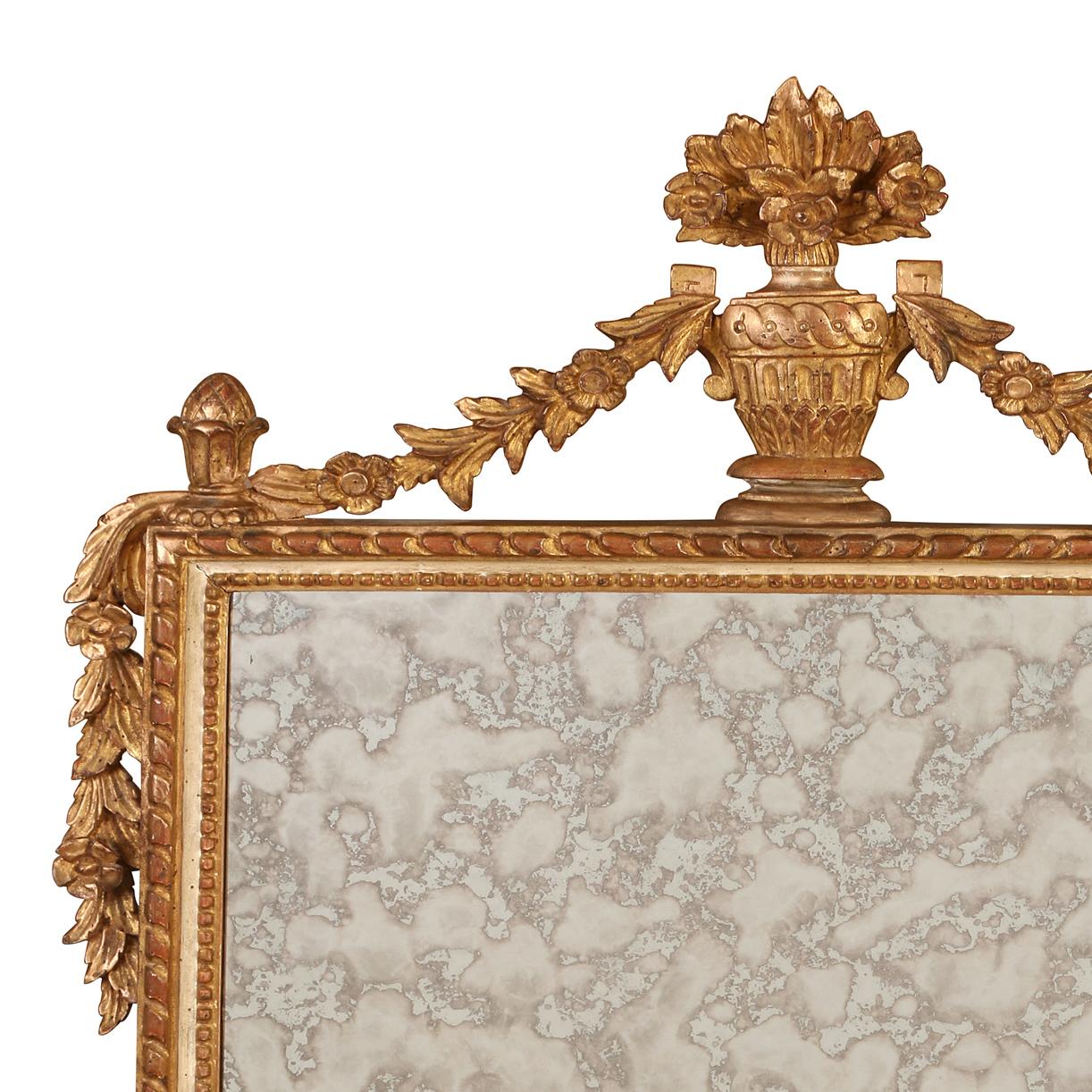Miroir néoclassique en bois doré avec une urne et des guirlandes au sommet, ce miroir présente un cadre méticuleusement sculpté qui respire la sophistication. La finition dorée ajoute une touche de régalité et d'opulence à la pièce, reflétant la