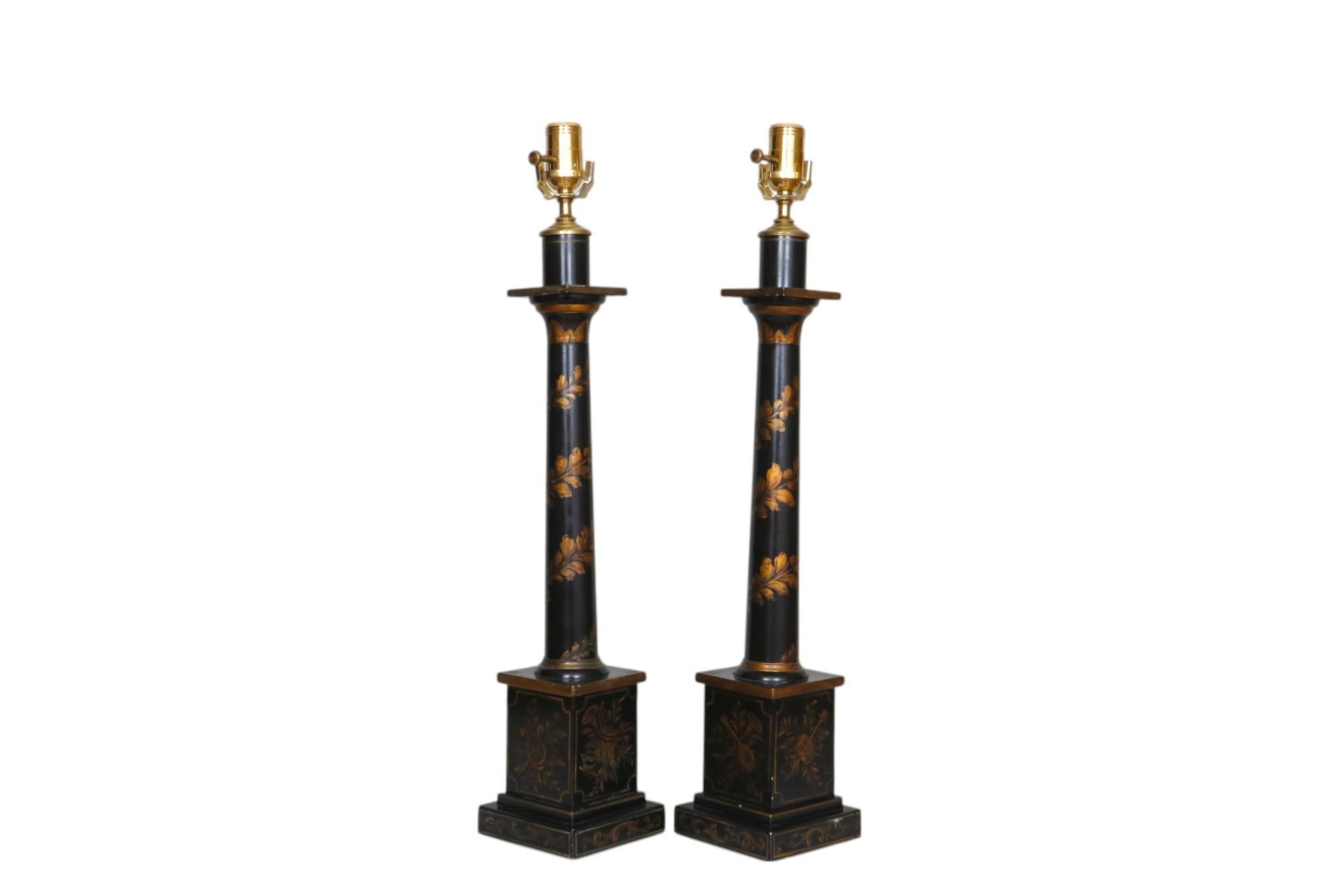 A pair of American Neoclassical style hand-painted tole table lamps. Painted black with gilt musical instruments on each side of the block base and foliage wrapped around the central columns. Label reads “Arrowsmith, Millbrook, N.Y.” underneath.