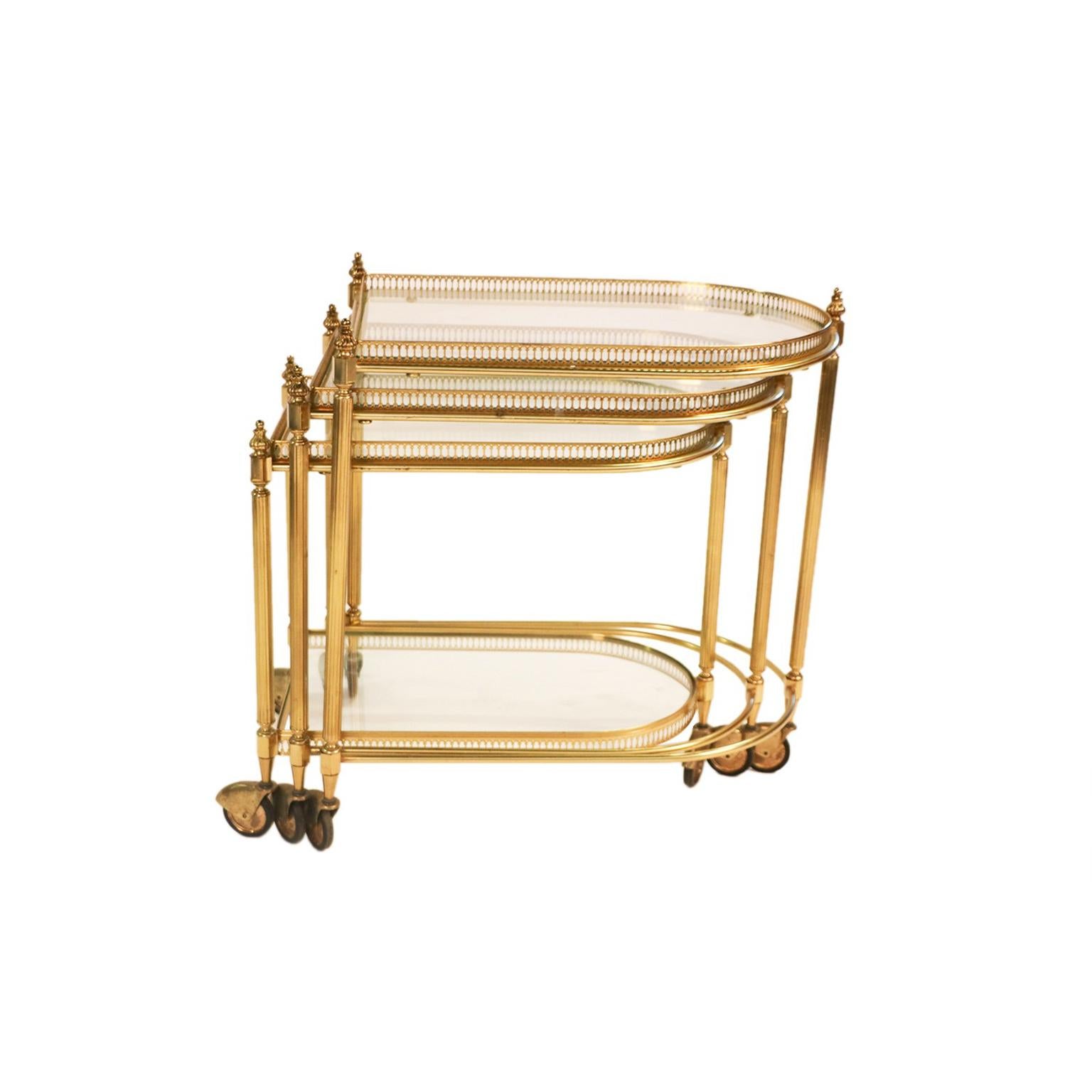 Set of three neoclassical, Hollywood Regency brass, and glass nesting tables on casters, exceptionally well crafted, circa 1940s. Featuring gallery trays with glass insert, resting on polished brass frames, accented with brass finials giving the set