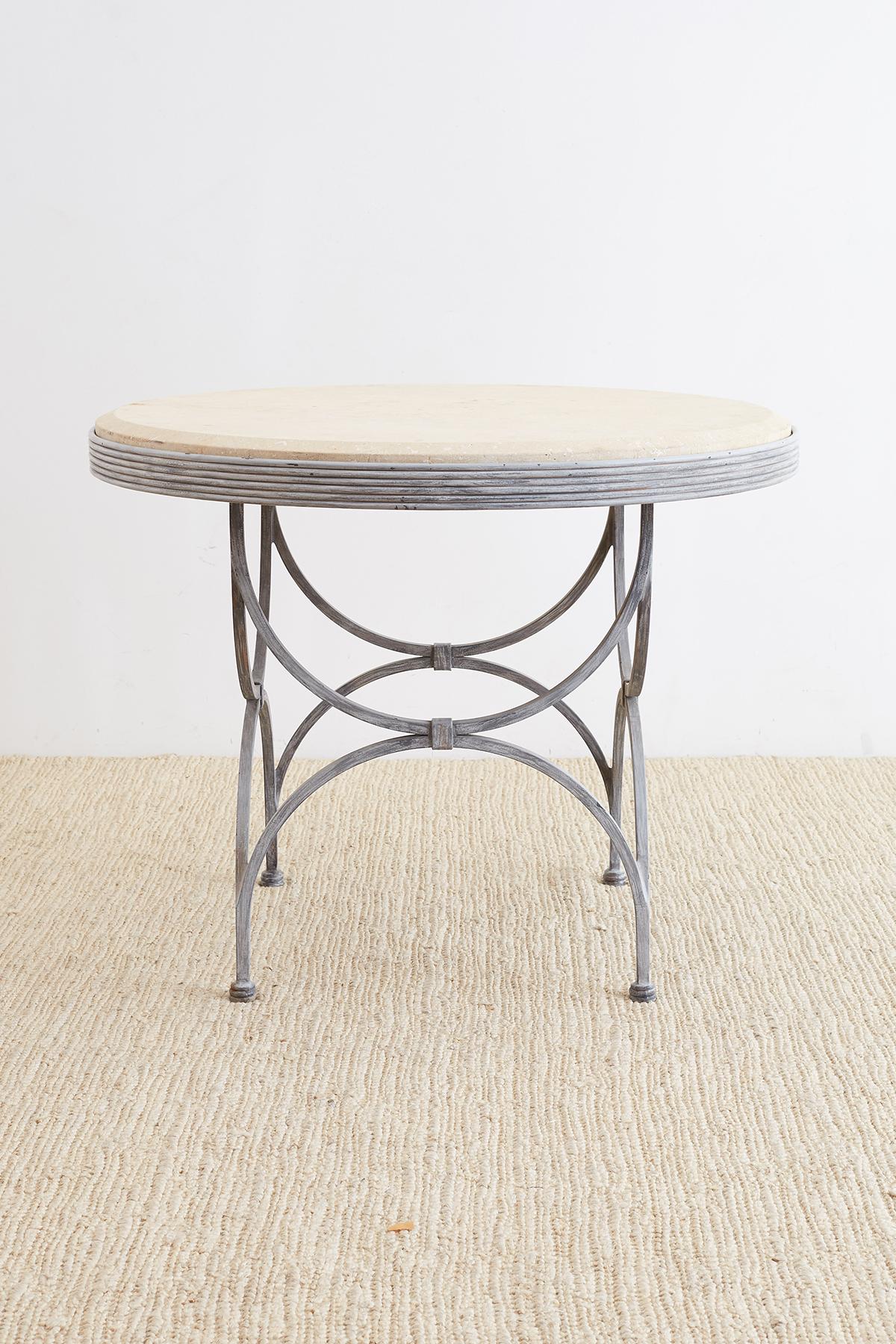 Extraordinary iron and stone patio garden table made in the neoclassical taste. Features a thick molded stone top with a beveled edge. The elegant base has a reeded edge and is supported by curved curule style legs conjoined on top and bottom.