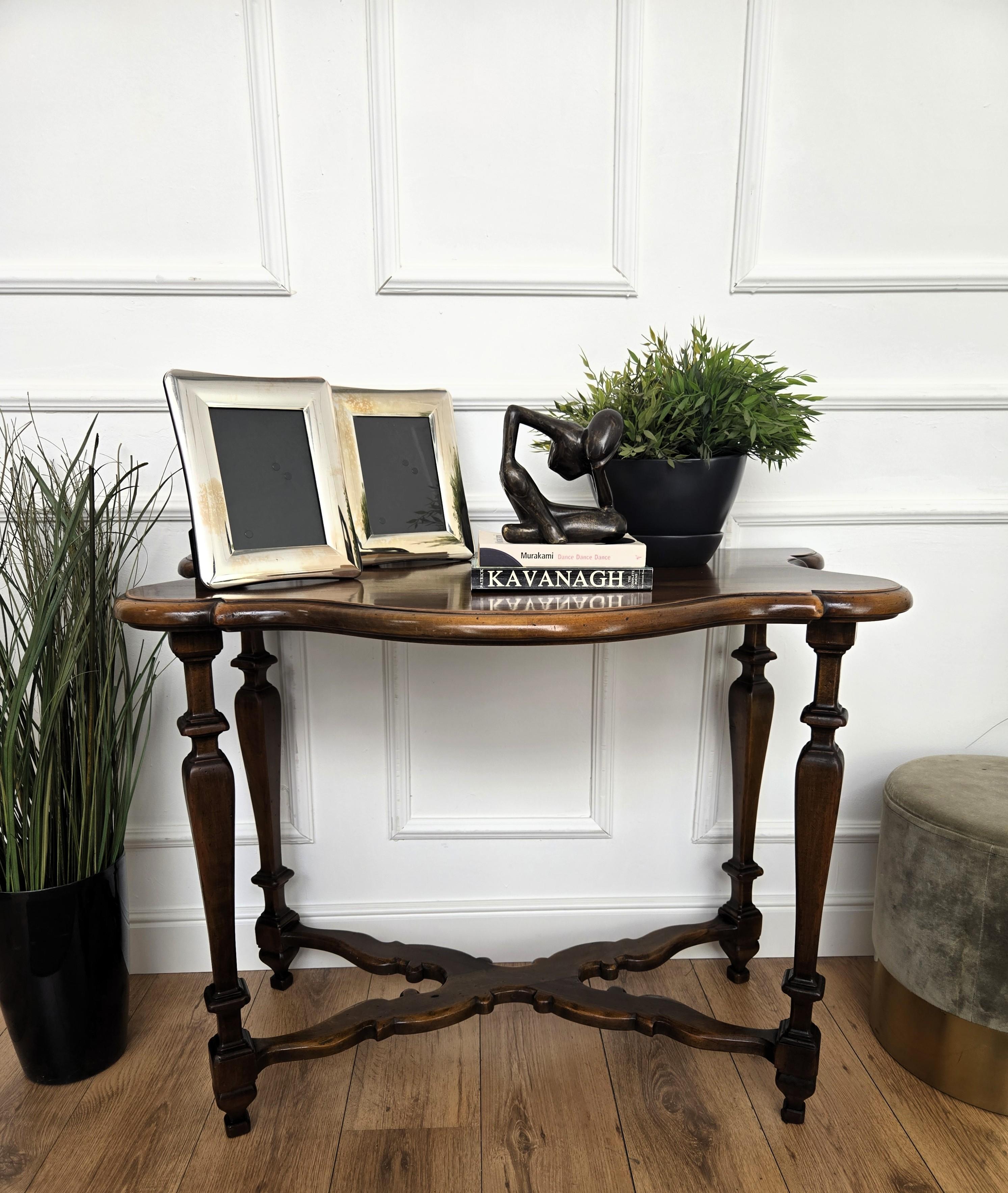 A beautiful Italian neoclassical walnut console table with serpentine shaped and beveled top, carved turned legs united by the classic shaped stretcher. 