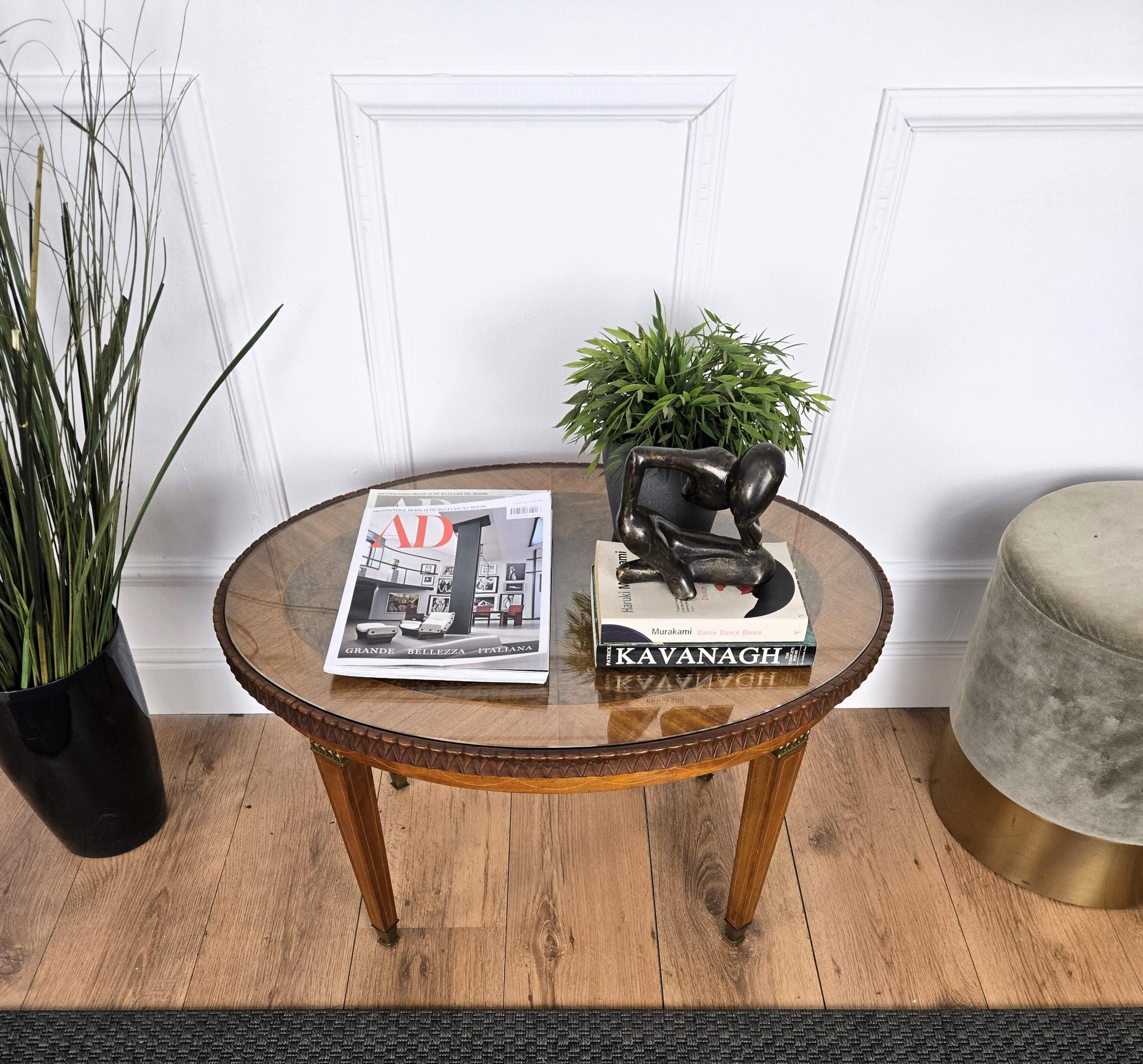 A beautiful Italian walnut side table with great details and frames, oval shaped with beautiful wood burl top covered in glass and side and legs inlay decors in classic figures completed by the brass finials. A very elegant, modern and classic piece