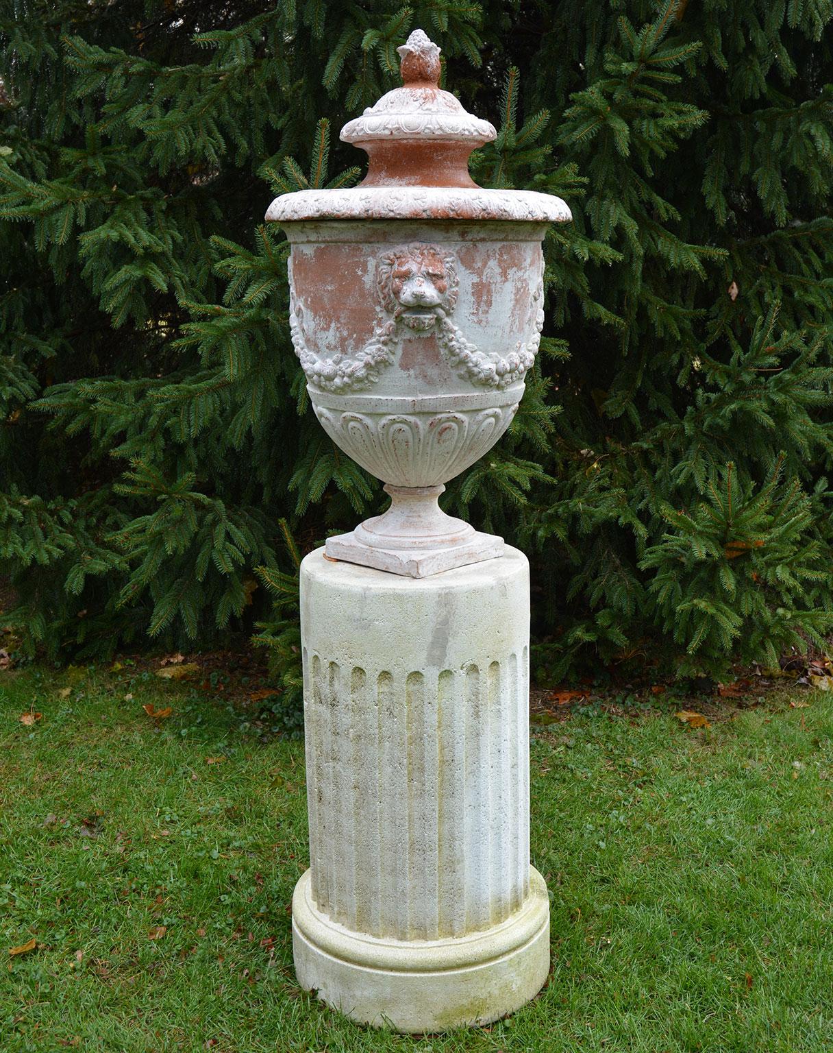 A lidded terracotta urn, with whitewashed finish, the body with floral and ribbon swags and lion masks, the lid with adapted egg-and-dart and acanthus leaf motifs, French, ca. 1880, on associated composition stone fluted columnar base, American, ca.