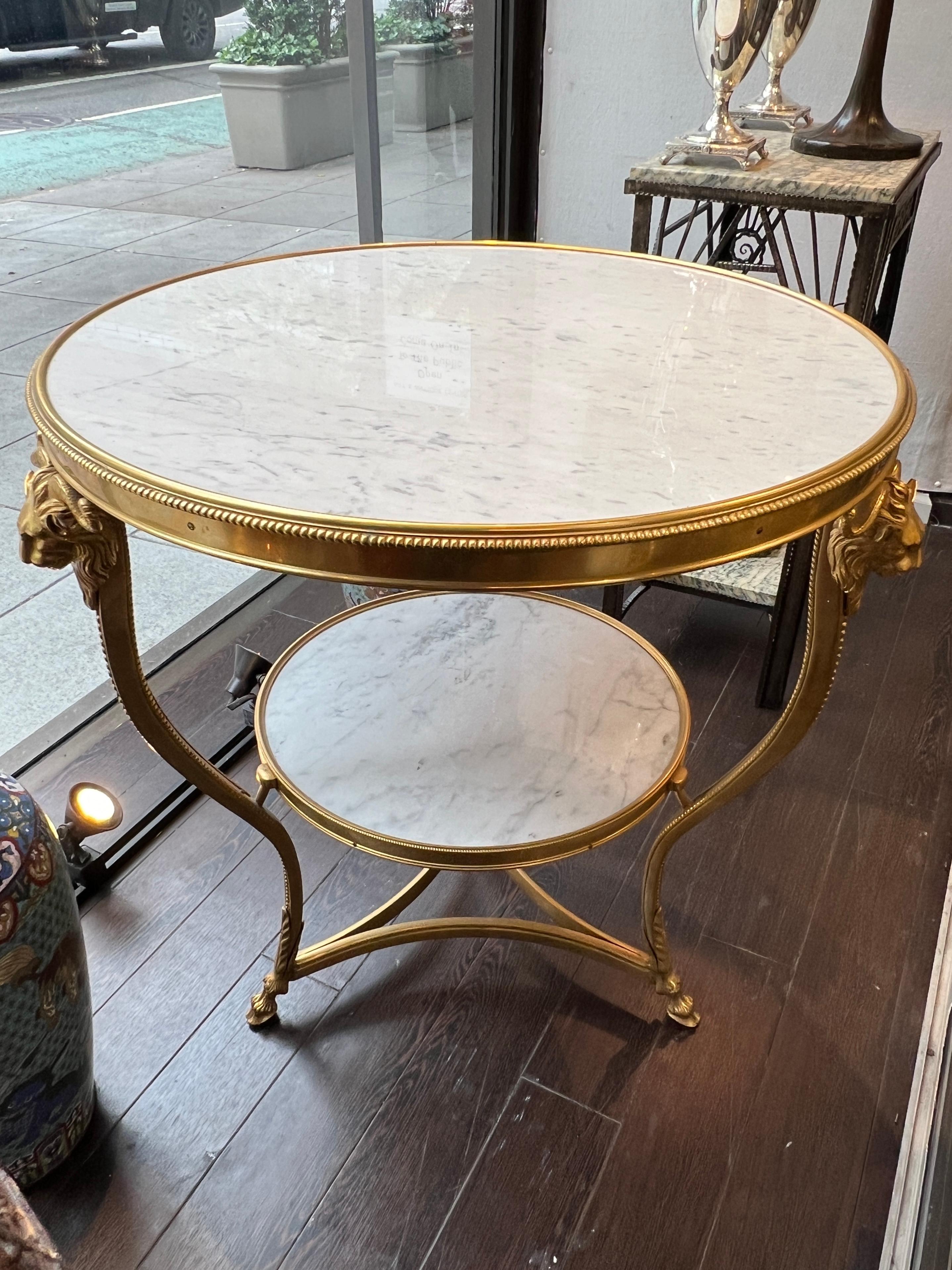 Our vintage gueridon form center table with white marble top and stretcher with streaks of light grey measures 30 inches across and 28 inches tall, and has a gilt bronze frame with beading at the edge, horned animal masks at the shoulder and hoof