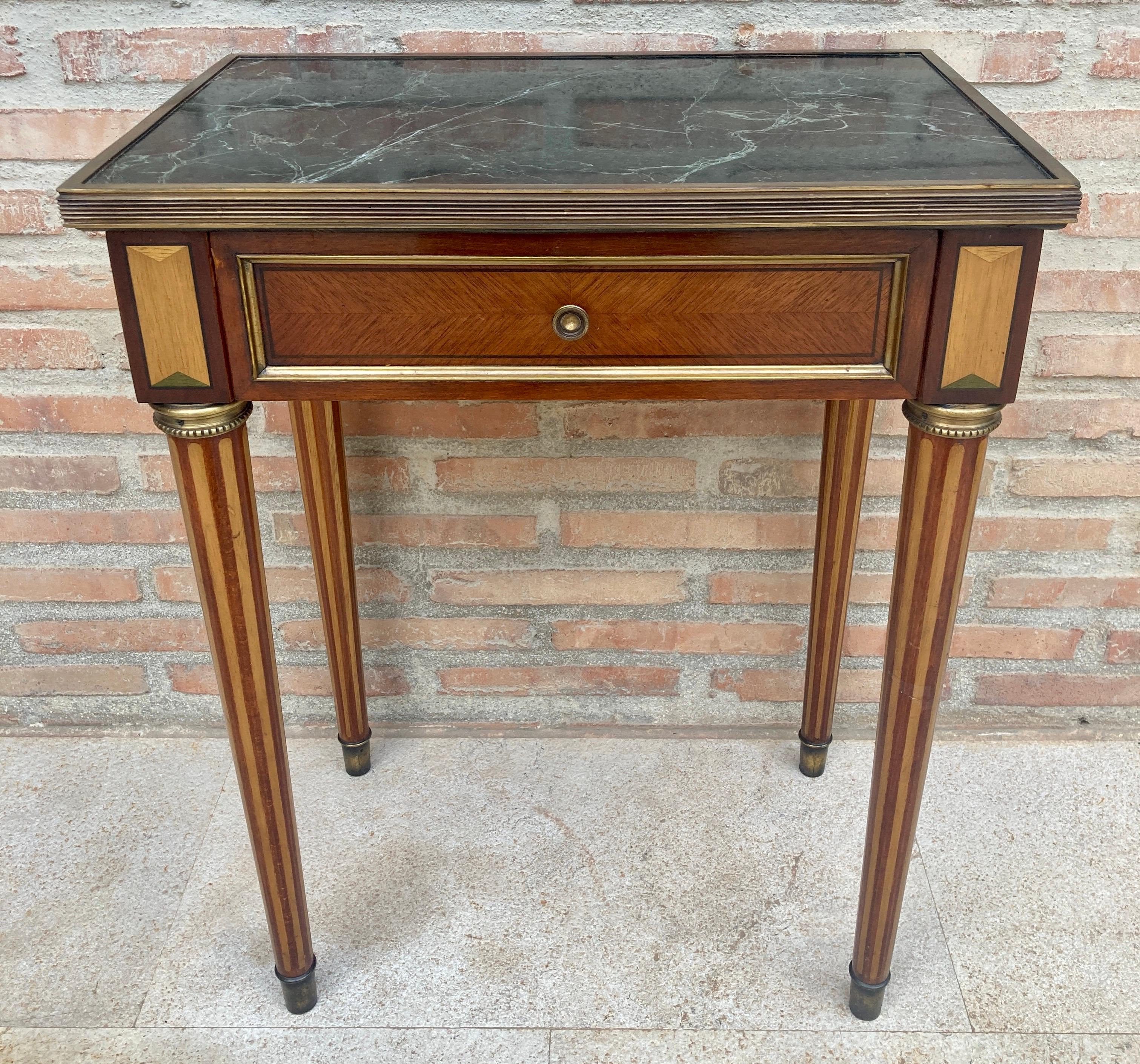 Unusual early 20th century neoclassical style rectangular side table with fluted legs and green and white marble. 
It has a drawer with its bronze handle and the lower part of its fluted legs is decorated with brass caps.
This charming table is an
