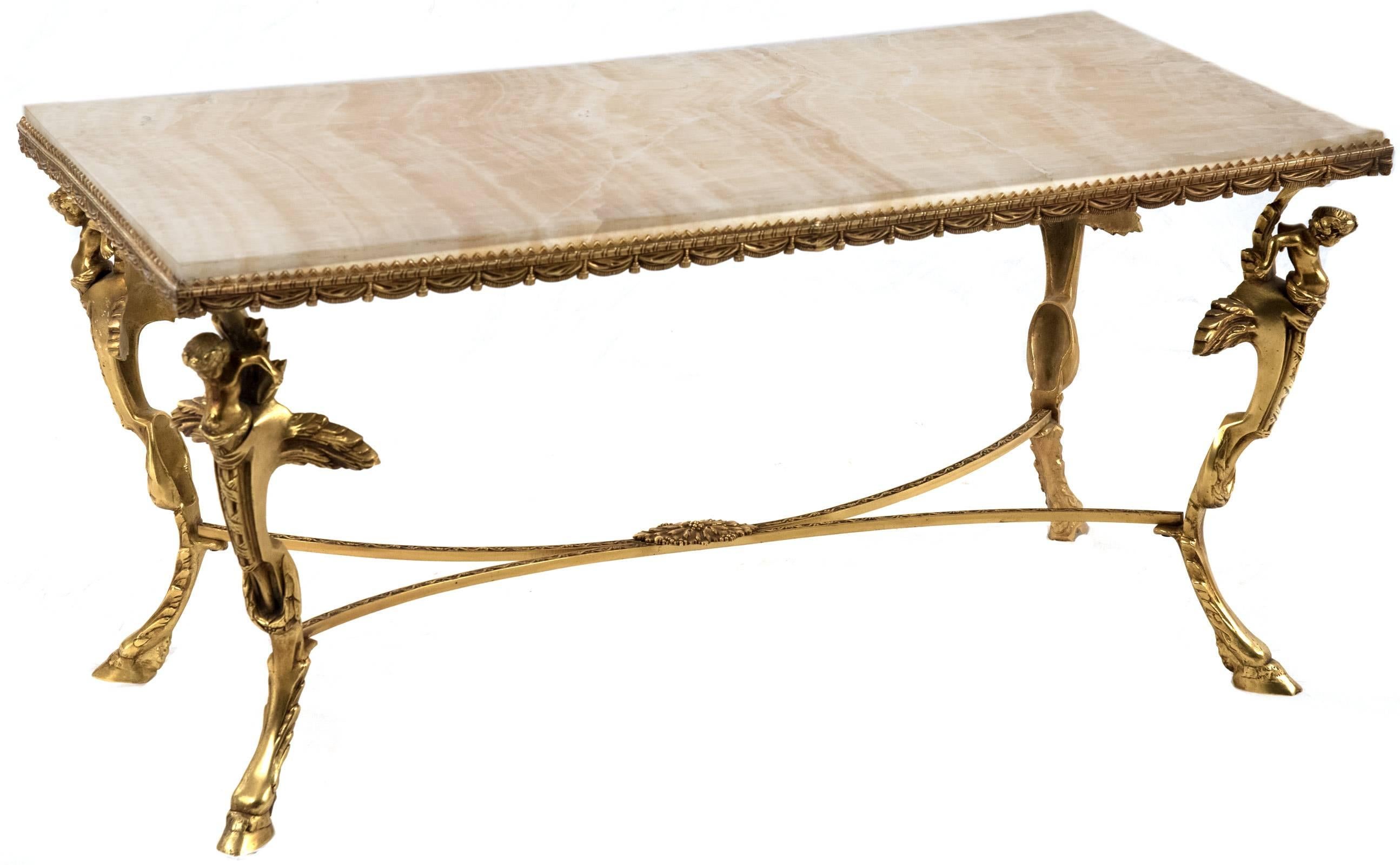 A marble and gilt neoclassical style coffee table with a veined marble top trimmed with stylized gilt fabric swaths raised on four legs with winged cherubs above a hoof foot, all joined by a rounded and incised X-frame stretcher with a central