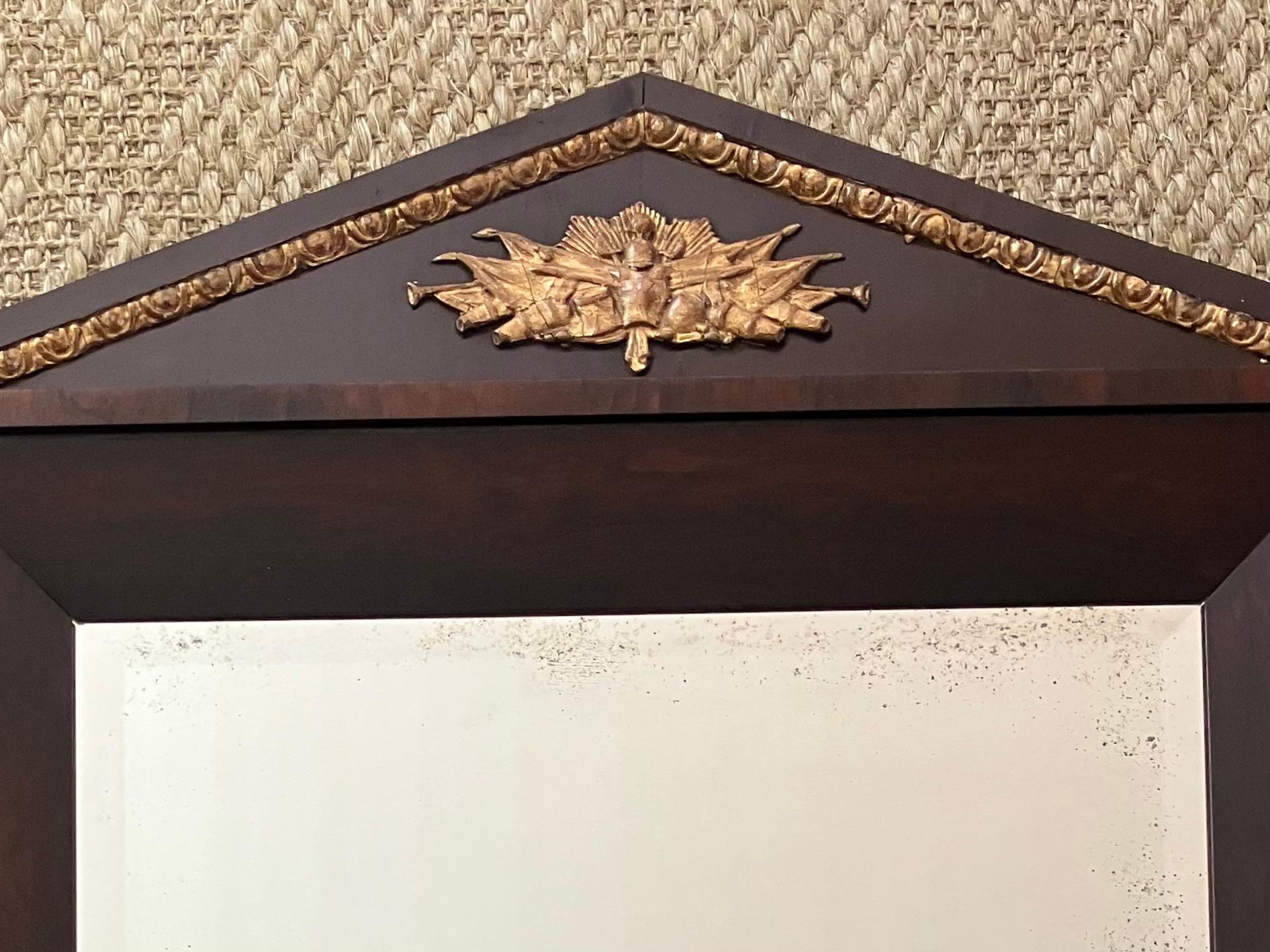 Specchio neoclassico militare in palissandro. Grande cornice in palissandro antico e intagliata in oro con ampio bordo smussato che incornicia lo specchio mercurio antico smussato sottostante  frontone intagliato e dorato che racchiude trofei