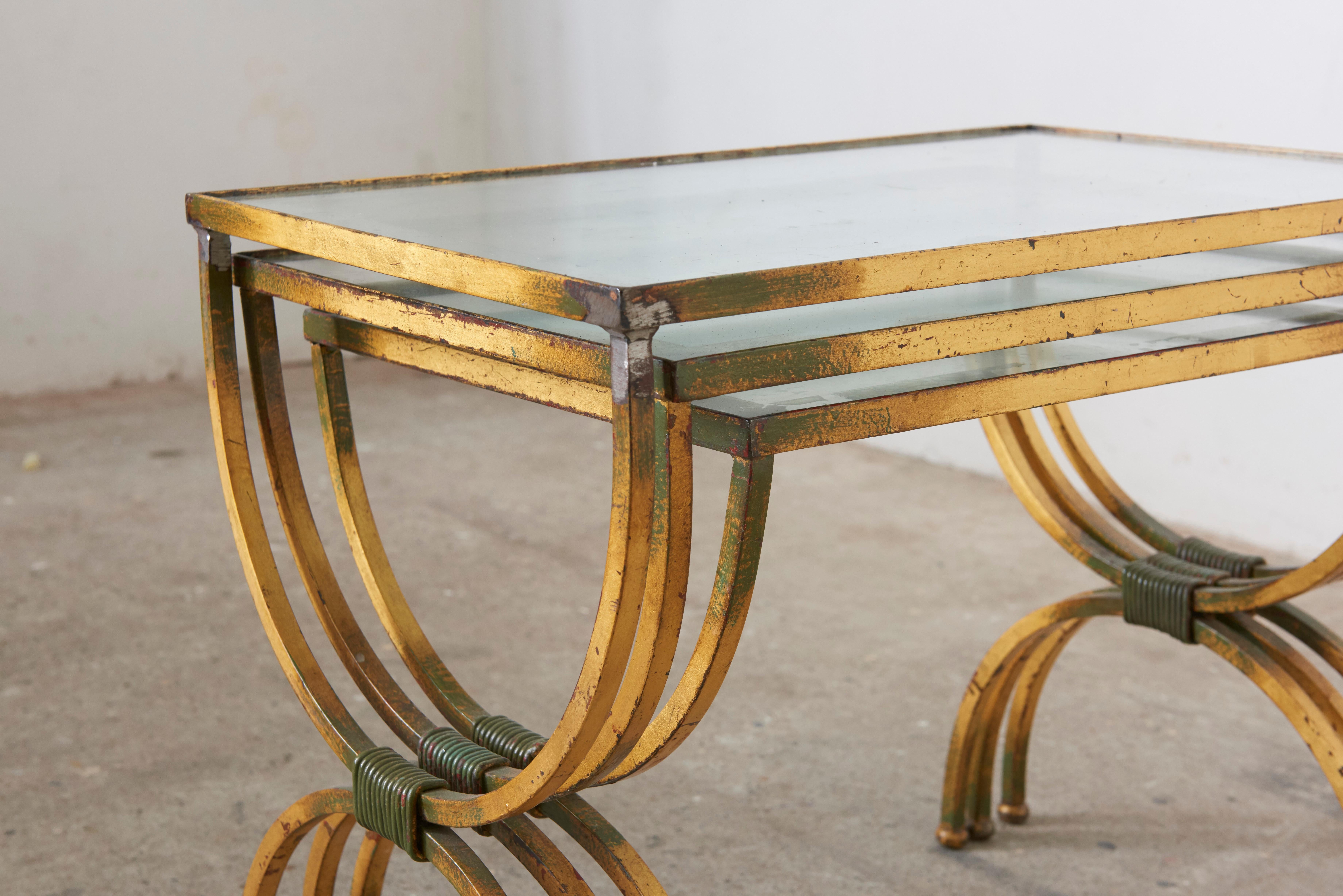 Set of tables in style of Jean Royere in the 1950s. The metal structure is hand gilt finished and has a gorgeous patina. 
The table tops are glass with a silver finish. All in good condition without any chips or cracks the silver with wear