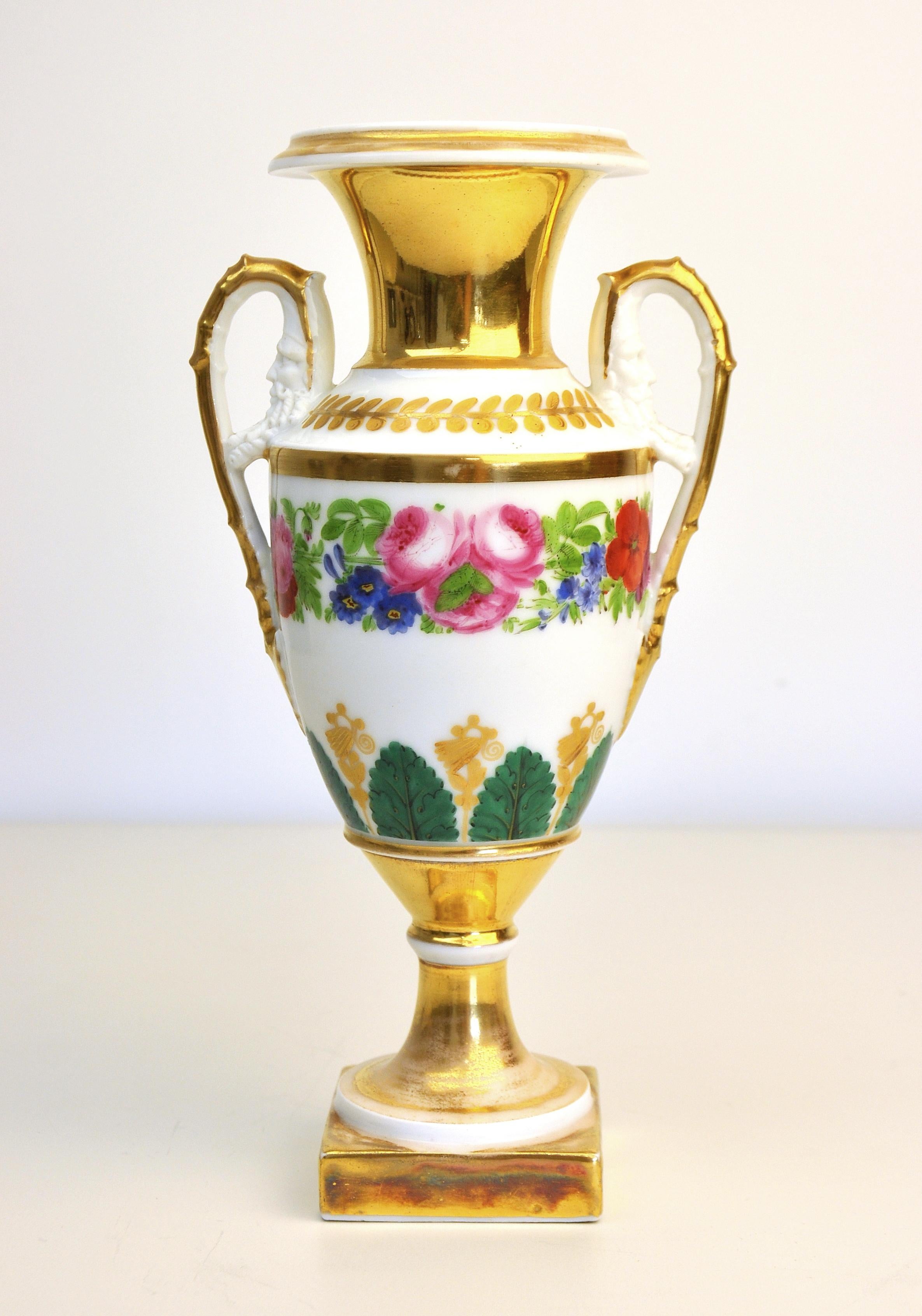 A fine and early Old Paris porcelain urn, dating from the late 18th-early 19th century. The partially gilt vase is abundantly hand painted with floral bouquets and acanthus leaves. It features a highly detailed mascherone under the gilt handles. A