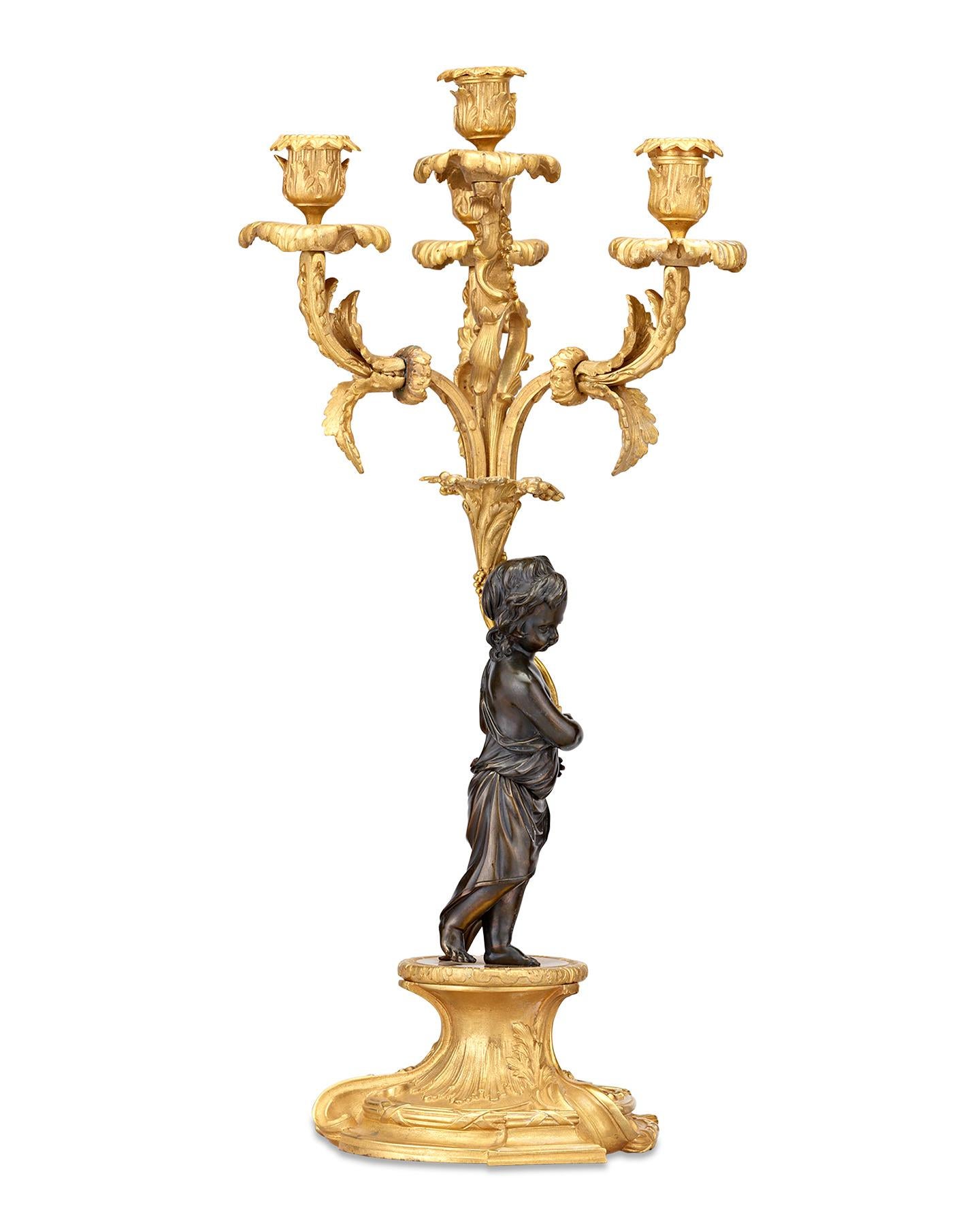 Crafted of bronze ormolu, these rare twin candelabra exhibit the beauty and grandeur of the neoclassical style. Two brushed-bronze putti figures donning classical-style togas support each candelabra, adding a charming touch exemplary of this