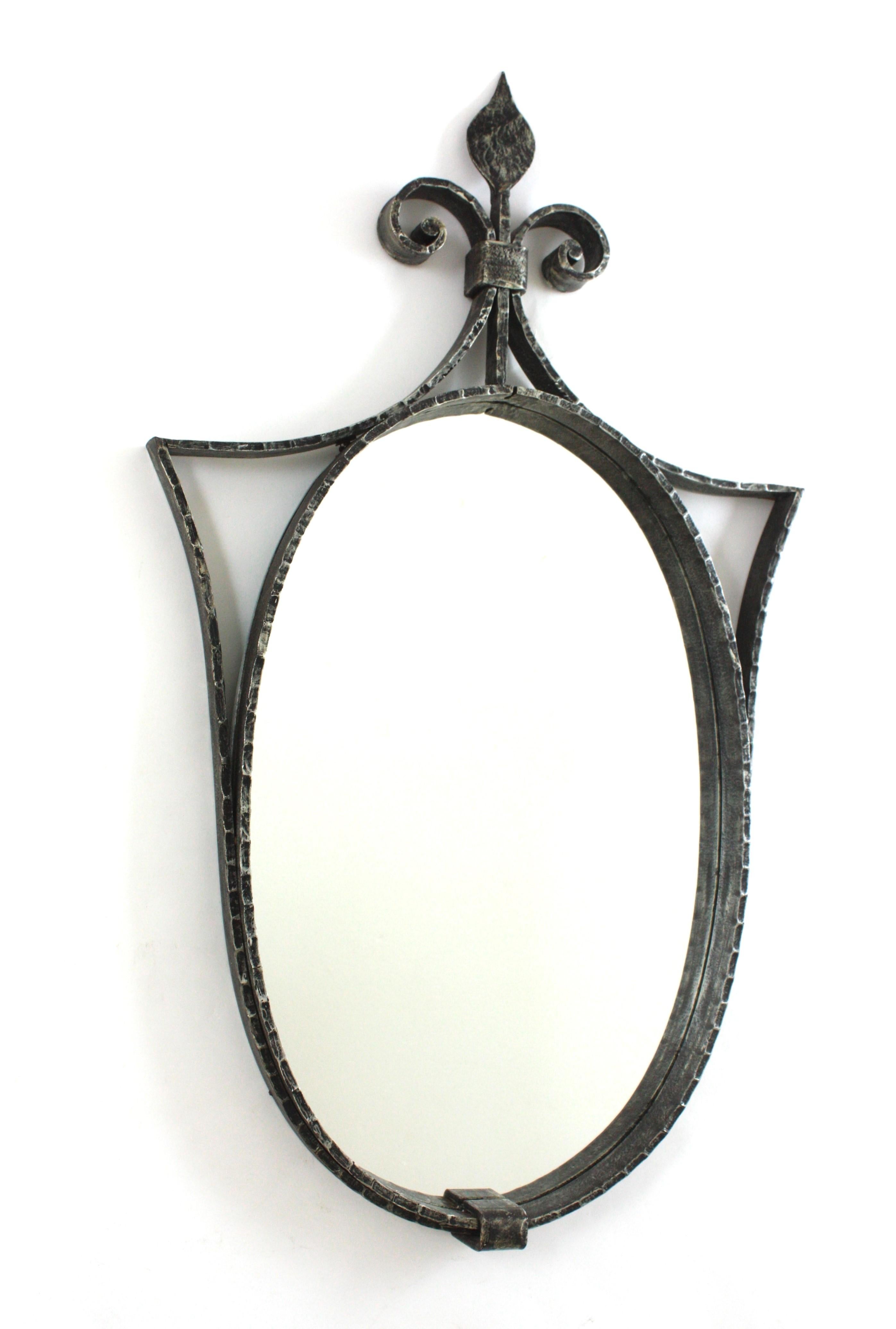 Hand Forged Spanish Mirror, Wrought Iron, Spain, 1940s.
Gorgeous wrought iron oval mirror with scroll details and spearhead or arrowhead crest. Manufactured at the Mid-20th century period in the style of Neoclassical.
Thick hand-hammered frame,