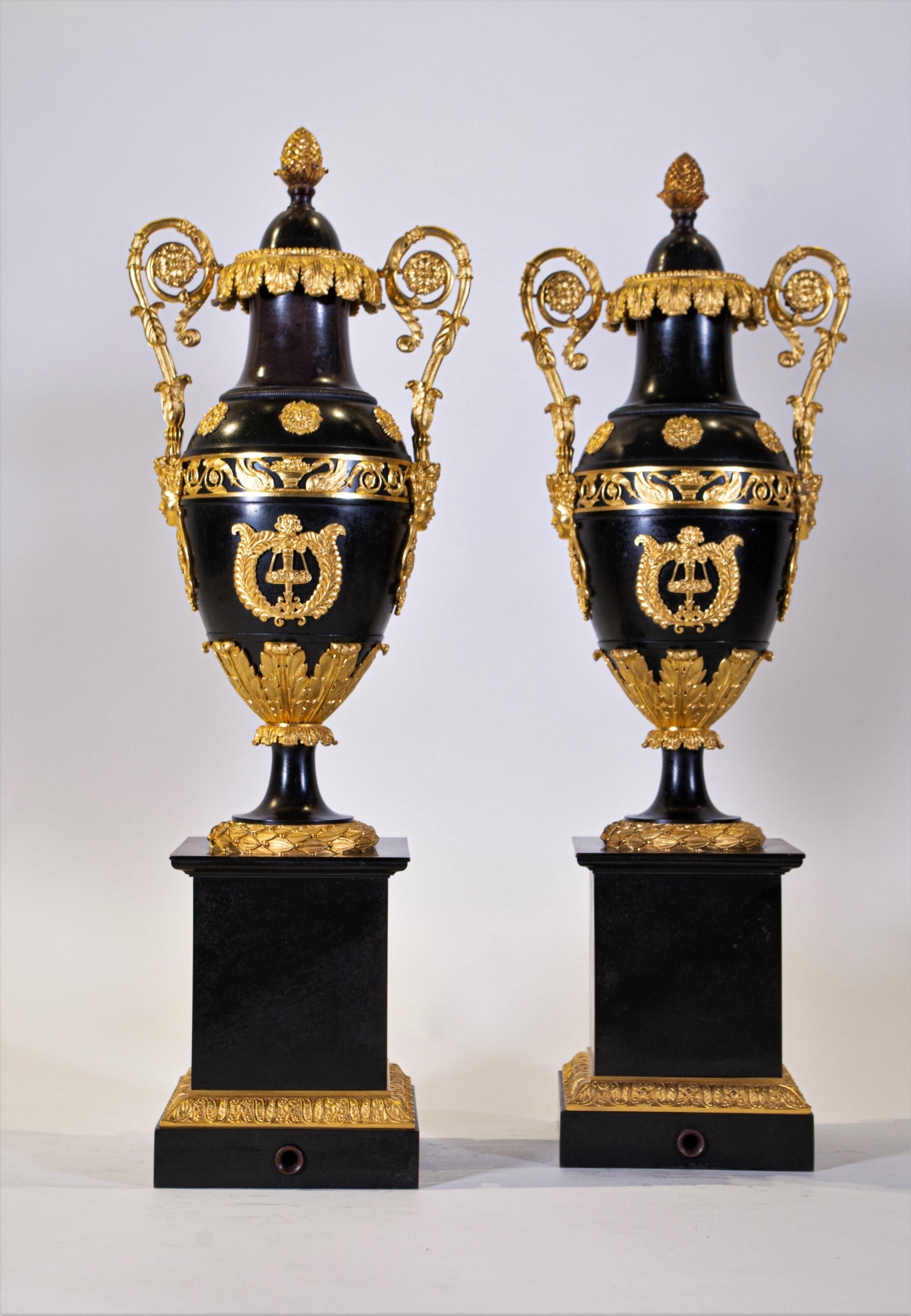 A gorgeous and rare neoclassical pair of patinated and doré bronze Empire period covered urns with doré bronze cupid masks and foliage scroll doré bronze handles. Each is beautifully cast and patinated in a rich dark black patina. Mounted on the