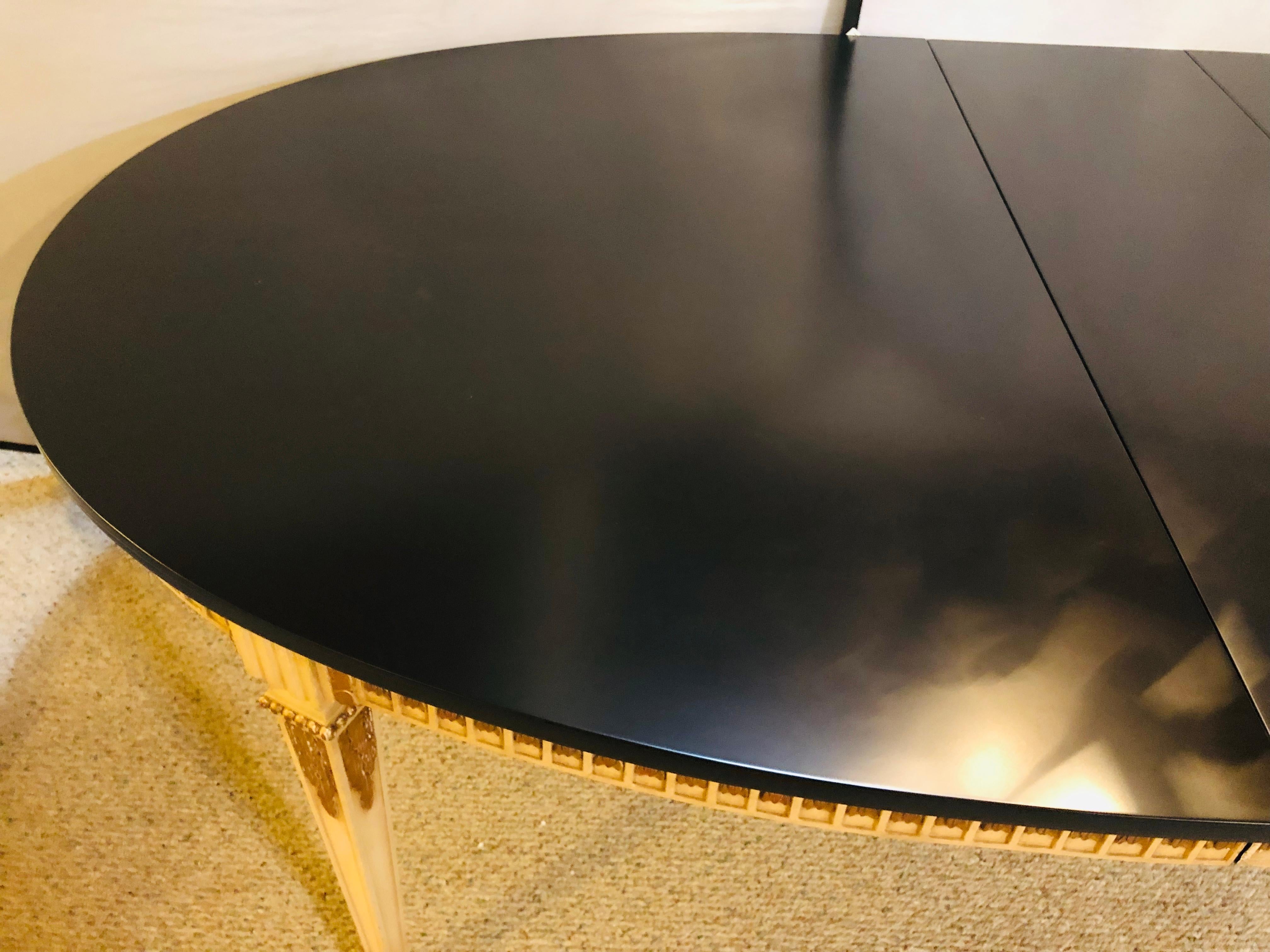 Neoclassical parcel-gilt and paint decorated dining table with ebony finished top. This table has one 16 inch width leaf with a full matching carved apron. The tabletop itself has been refinished. There is a retractable center leg as for added