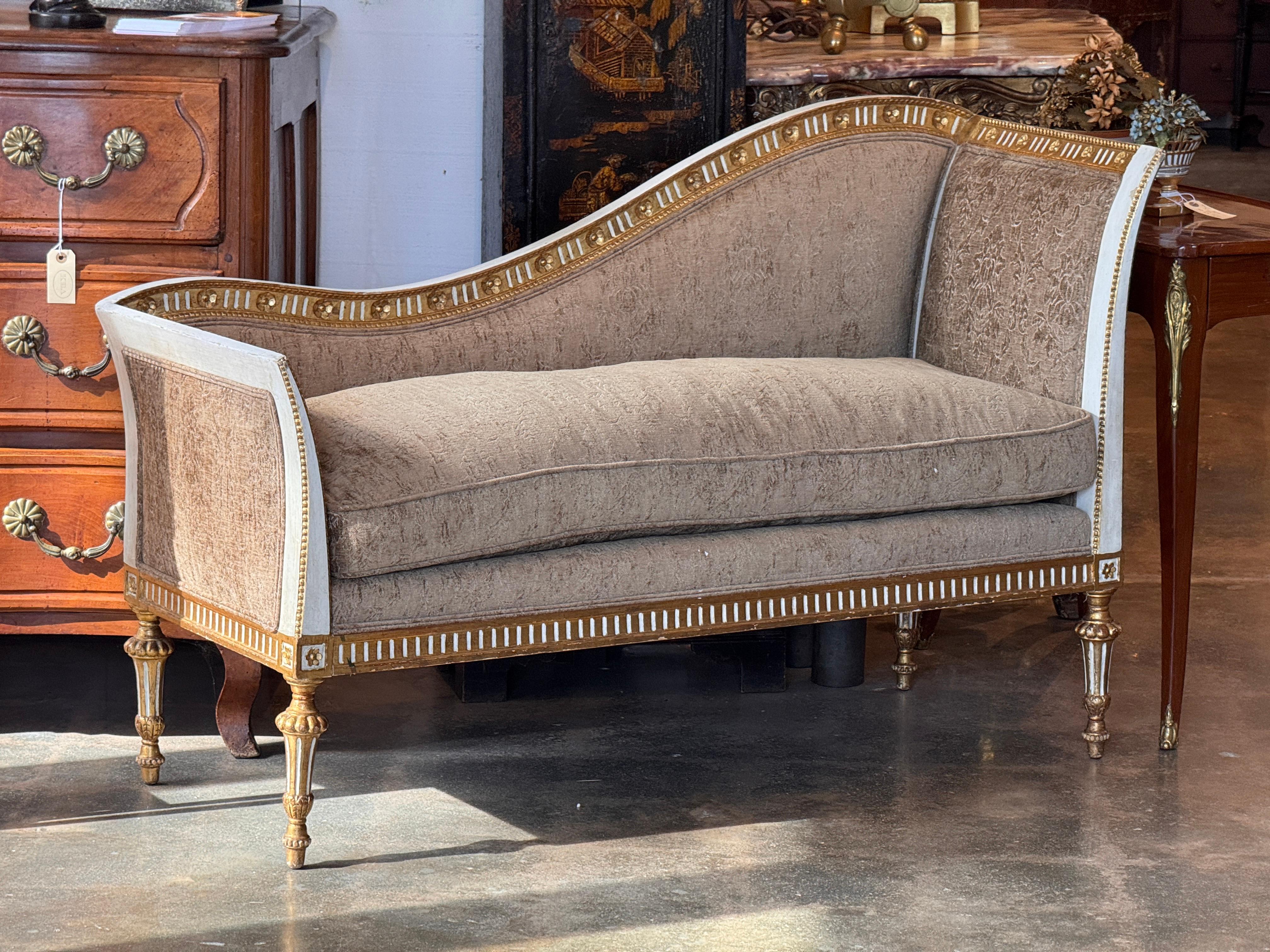 Divano neoclassico dorato a pacchi con un grazioso schienale asimmetrico e una cornice finemente intagliata con scanalature e dettagli floreali. La finitura dorata e verniciata mette in risalto gli ornamenti nitidi e le gambe tornite, completate da