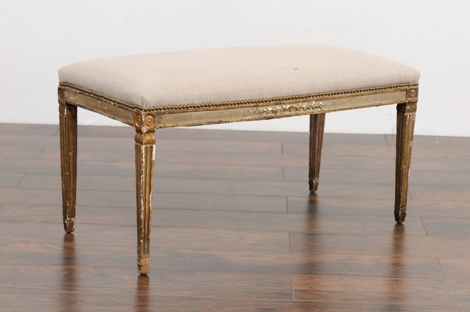 An Italian neoclassical period painted bench from the early 19th century, with foliage motif, tapered legs and new upholstery. This exquisite Italian Neoclassical bench features a rectangular seat, covered with a new linen fabric accented by a brass