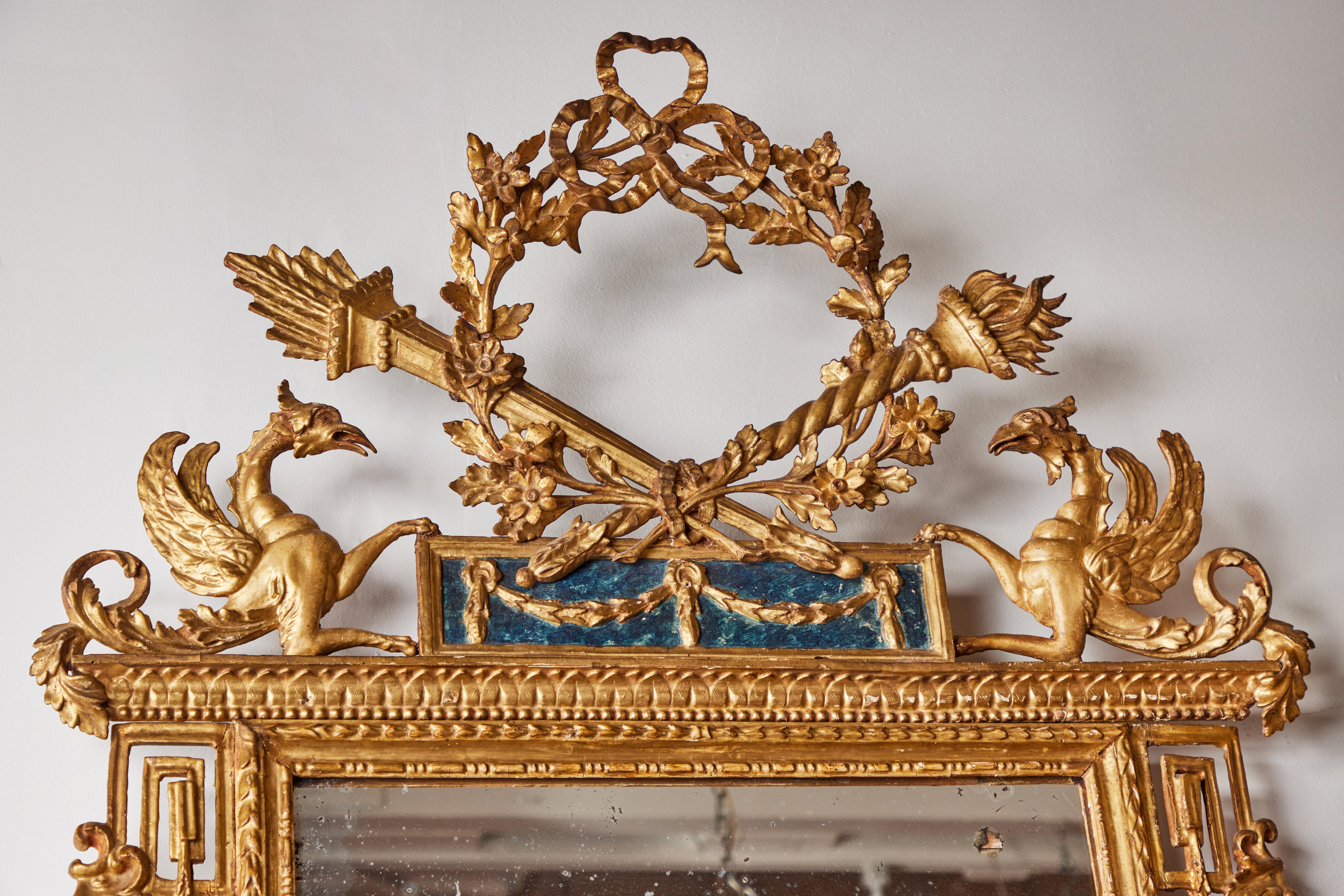 A pair of completely original, hand-carved and gilded, Italian, c. 1800 pier mirrors. Each featuring a spectacular crown consisting of a pierced, flower covered wreath surmounted by a bow, and flanked with lit torches. The wreath sits above a parcel