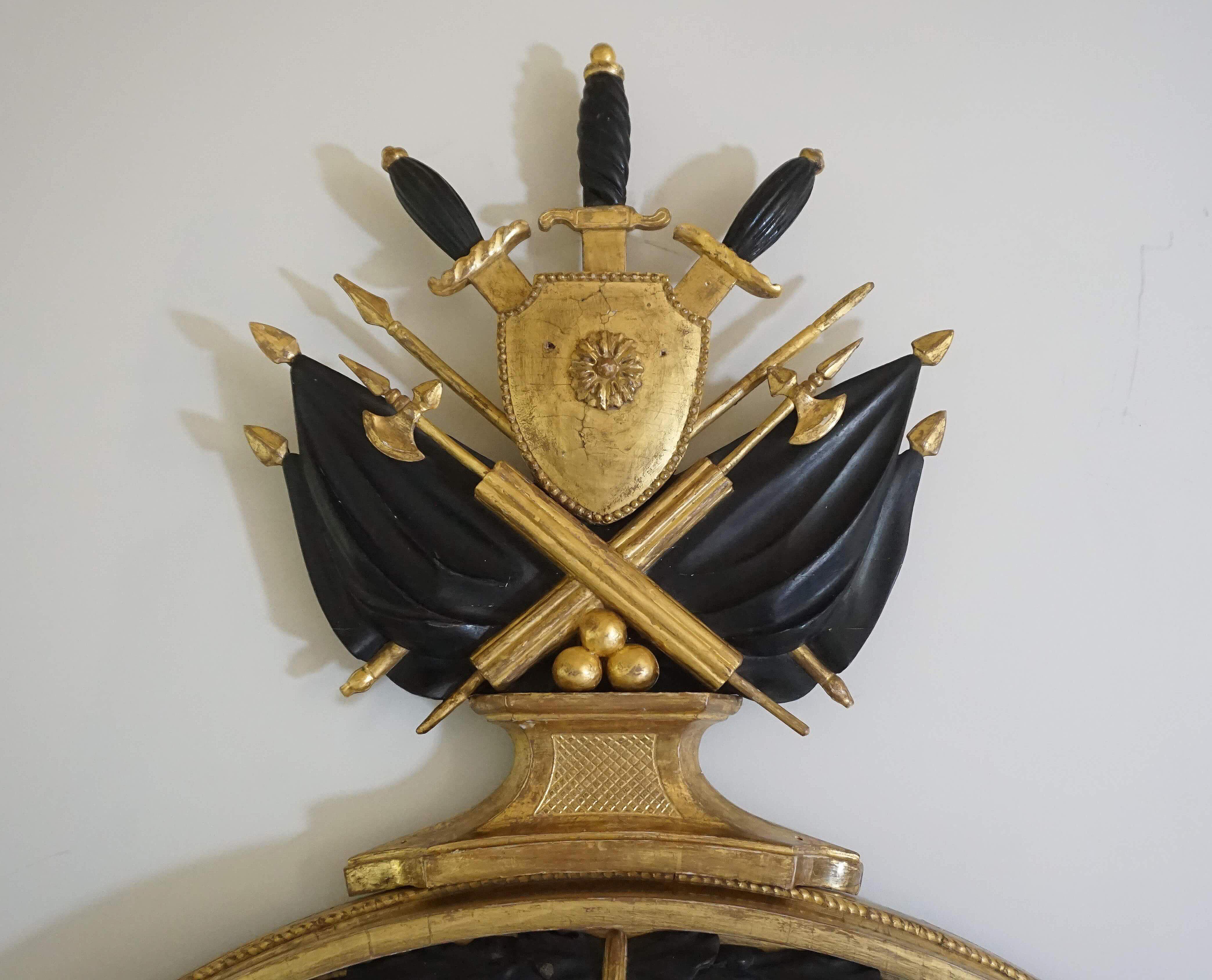 English regency period, possibly Irish, neoclassical style convex mirror of good size having giltwood and ebonized frame; the elaborate cresting with ancient Roman Army iconography of ebonized handled swords behind gilt shield above crossed fasces