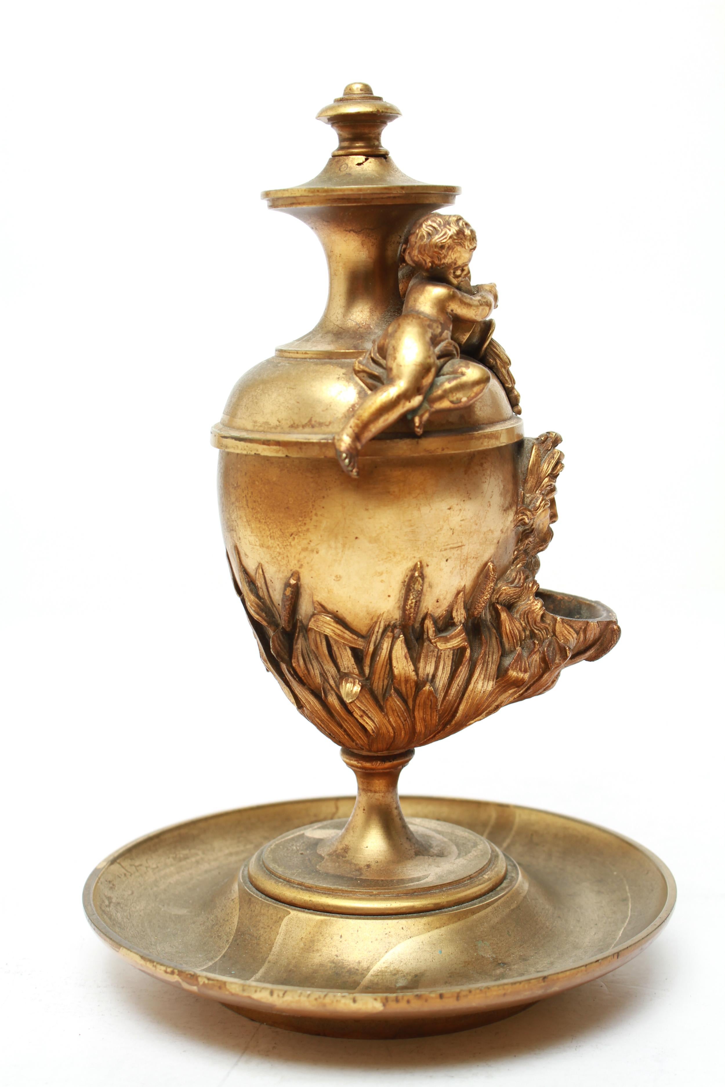 Neoclassical Revival gilt bronze figurative oil lamp in egg shaped receptacle with locking cover and spout. The piece has high relief putti, swags, a Classical head of a man, and cattails. In great vintage condition.