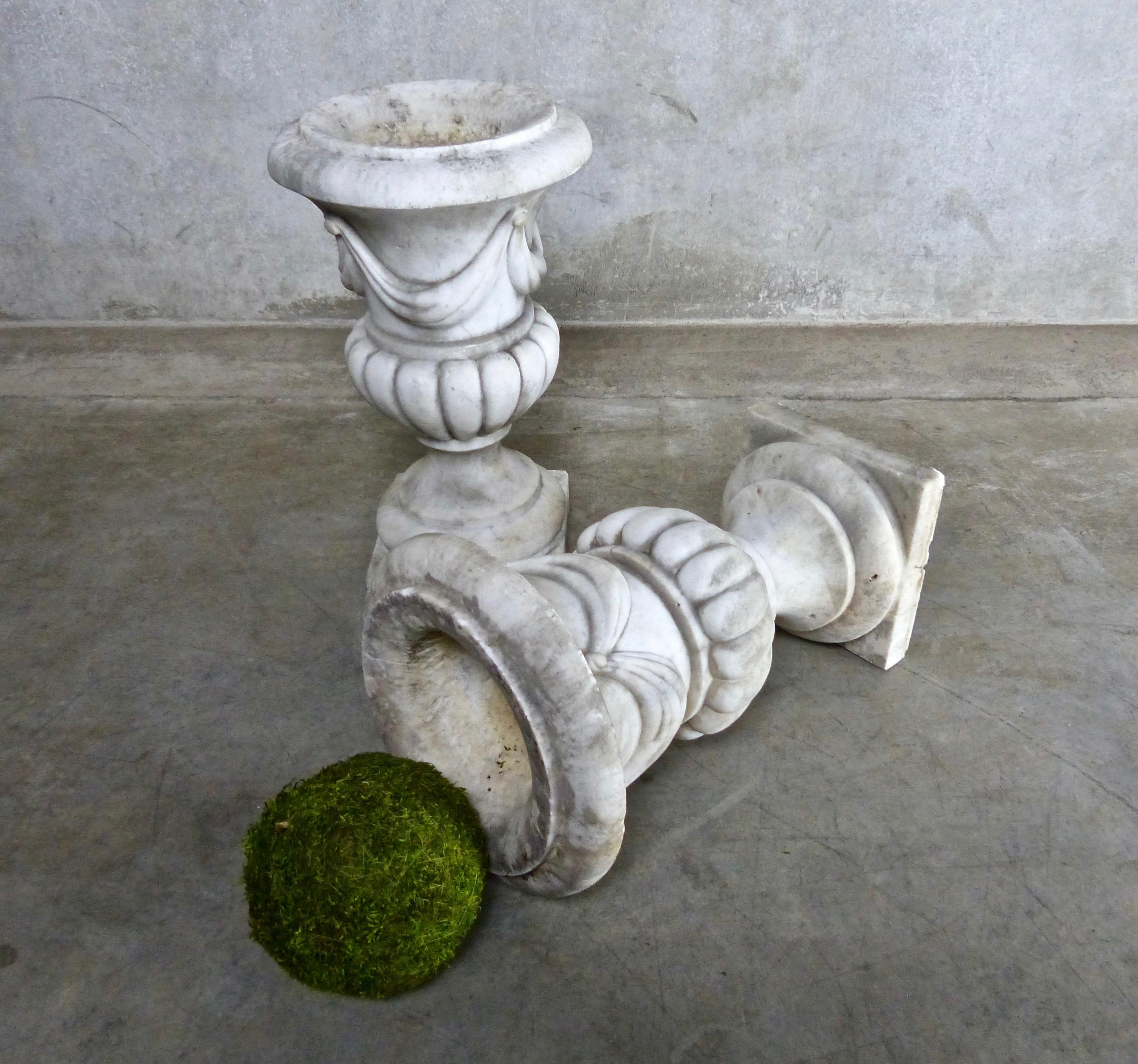 A matched pair of petite, hand carved, solid white marble garden urns/planters/jardinières. Neoclassical Revival Campana (bell-shaped) form with attached pedestal base. Dimensions 17” height x 10” diameter.
 