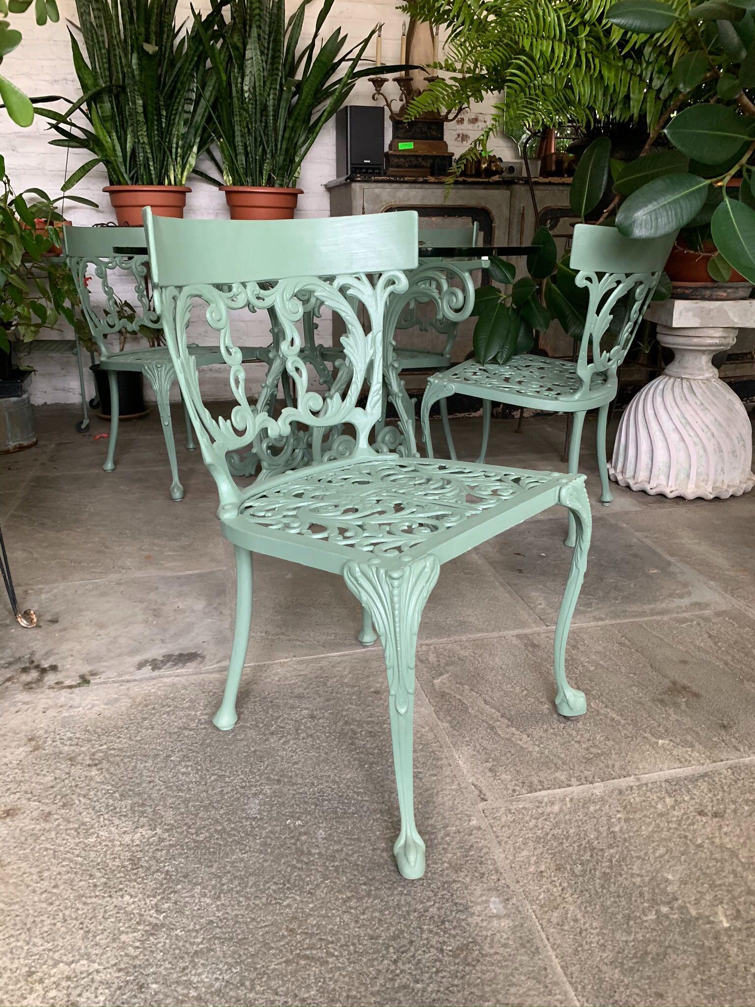 Cast iron outdoor garden or patio furniture with green painted finish. The set is composed of five pieces comprising one glass top table and four chairs in Neoclassical Revival style. In great vintage condition with age-appropriate wear and