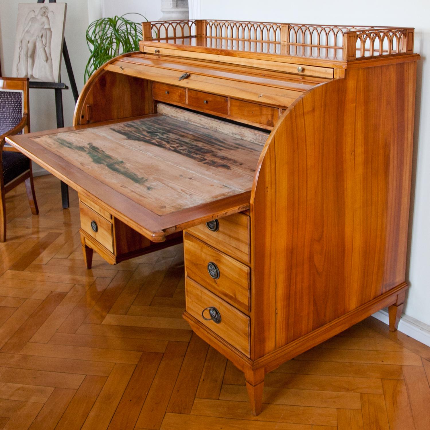Large roll-top desk out of solid cherry wood. The base with seven drawers stands on tapered legs. The top has one very slim pullout and a low arcade balustrade on three sides. The interior is made up out of four drawers. The desk is in its original