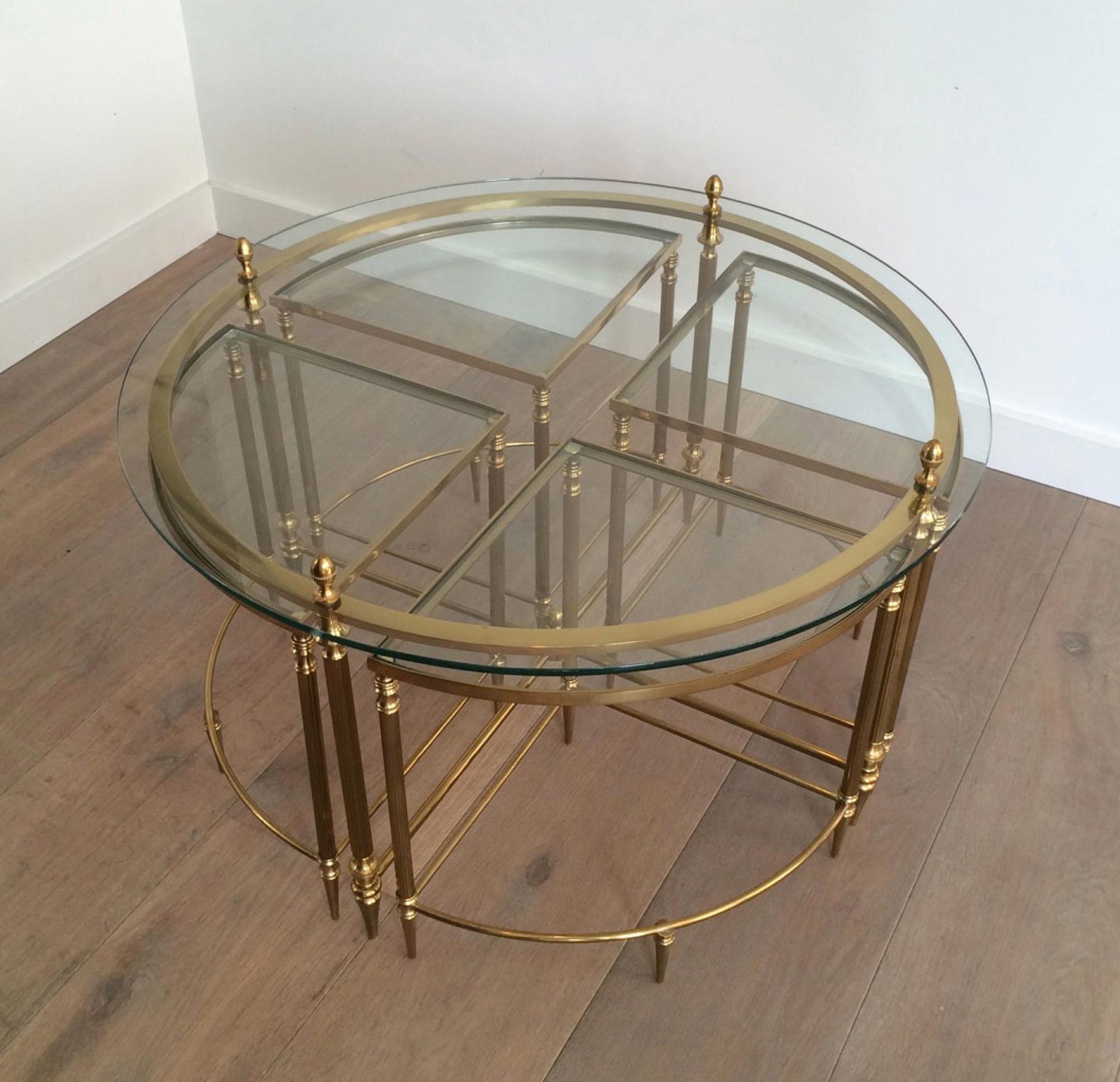This very nice neoclassical round coffee table is made of brass with a round glass top. Four corner nesting tables can slide under the main table. These corner tables are also made of brass with glass tops and can be used to enlarge the main table