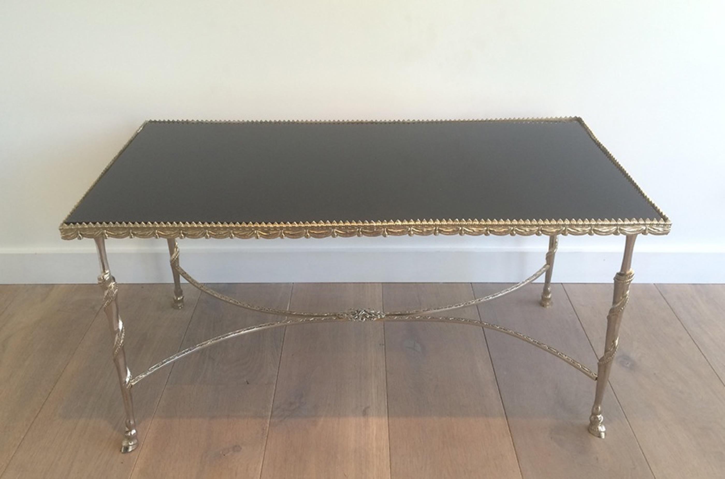 This very nice coffee table is made of a silver base with ribbons and animal feet and with a crown all around the top. The top of the cocktail table is made of a black lacquered glass top. This is a French work in the style of Maison Jansen, circa