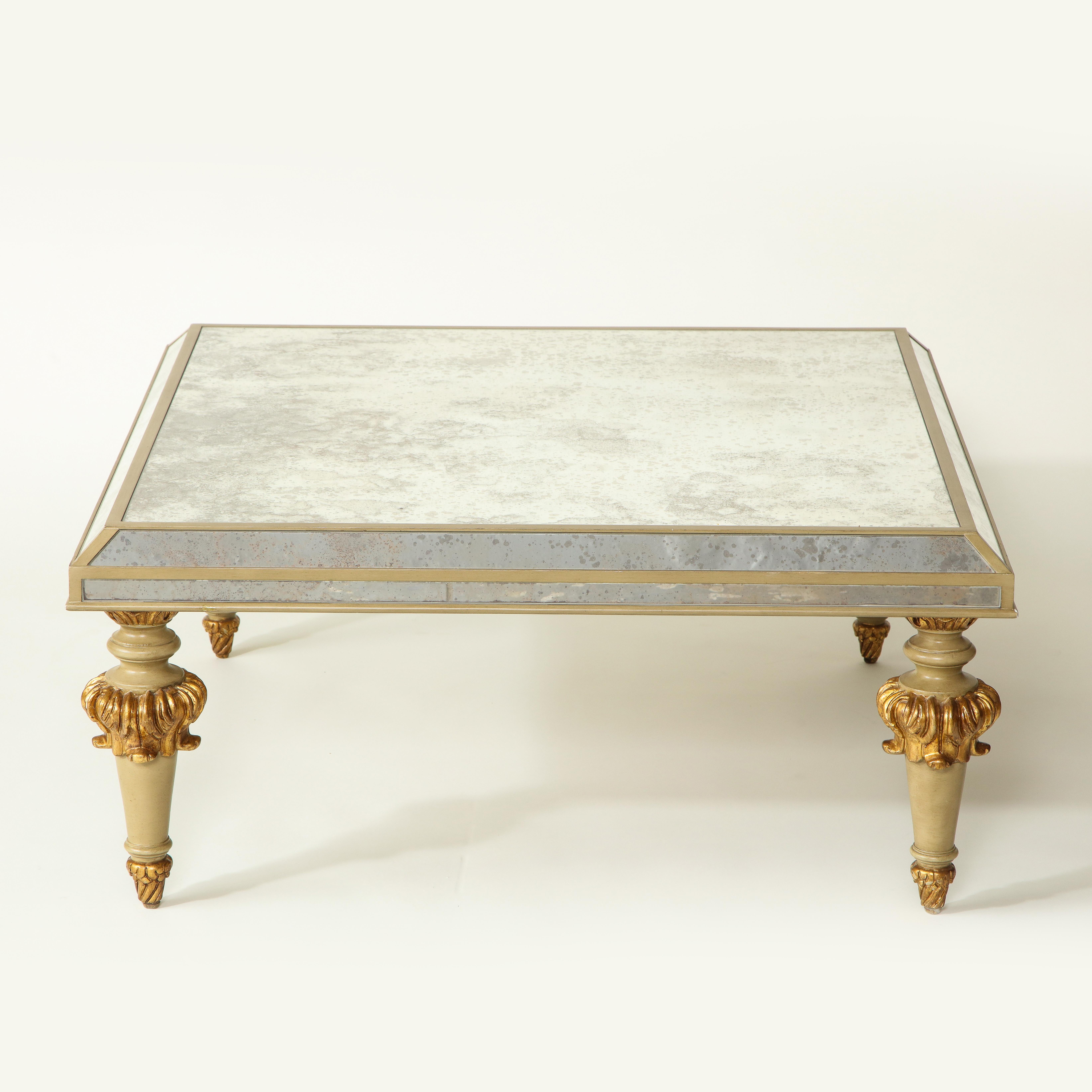The antiqued mirrored top with mirrored border glass edges raised on greige-painted tapering legs carved with gilt acanthus leaves.