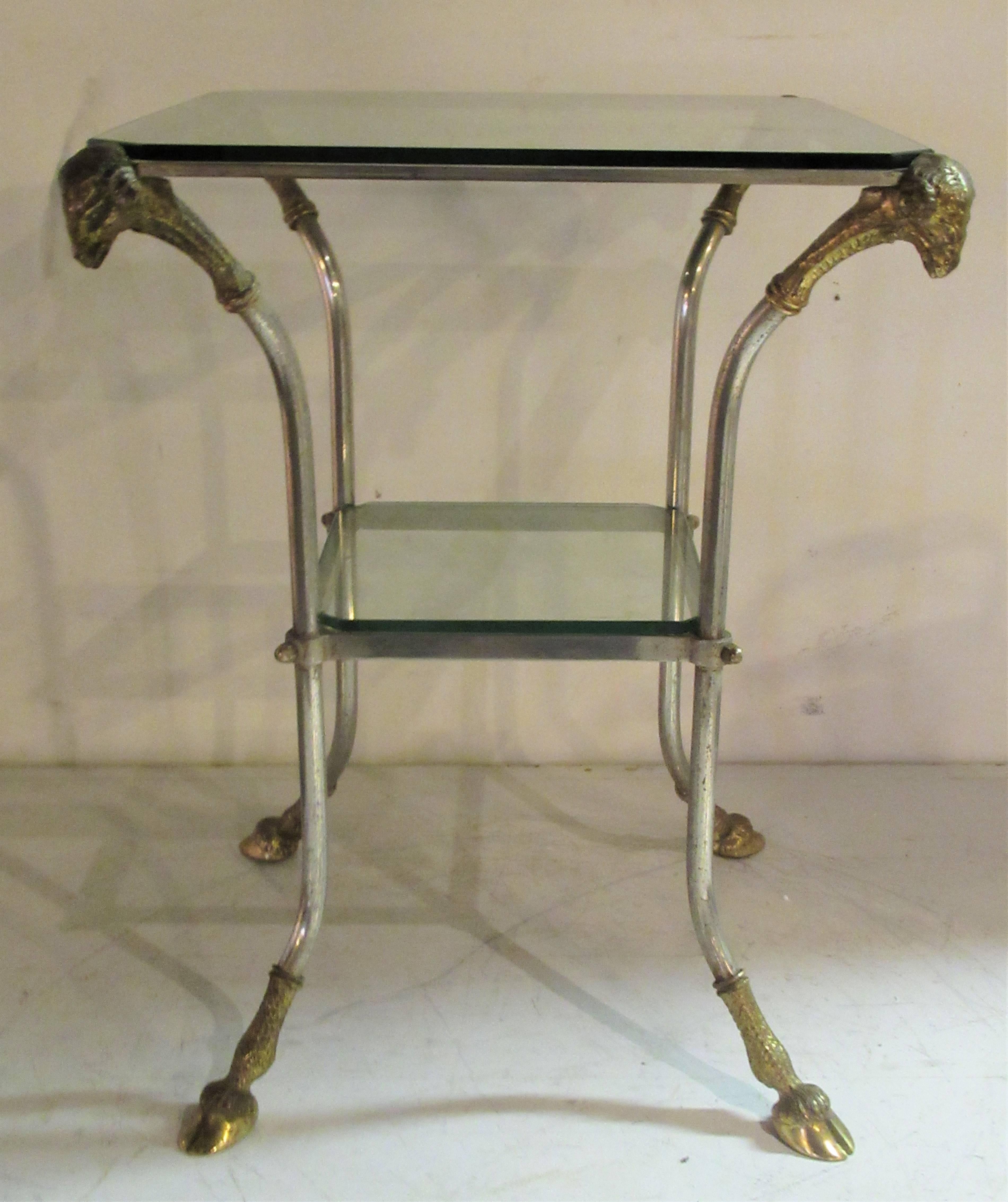 Neoclassical style steel frame two tier fitted plate glass table ( glass top / lower shelf with glass - see picture 2 )  with large gilt brass bronze rams heads and cloven hoof feet. Italian - in the style of Maison Jansen, circa 1960.