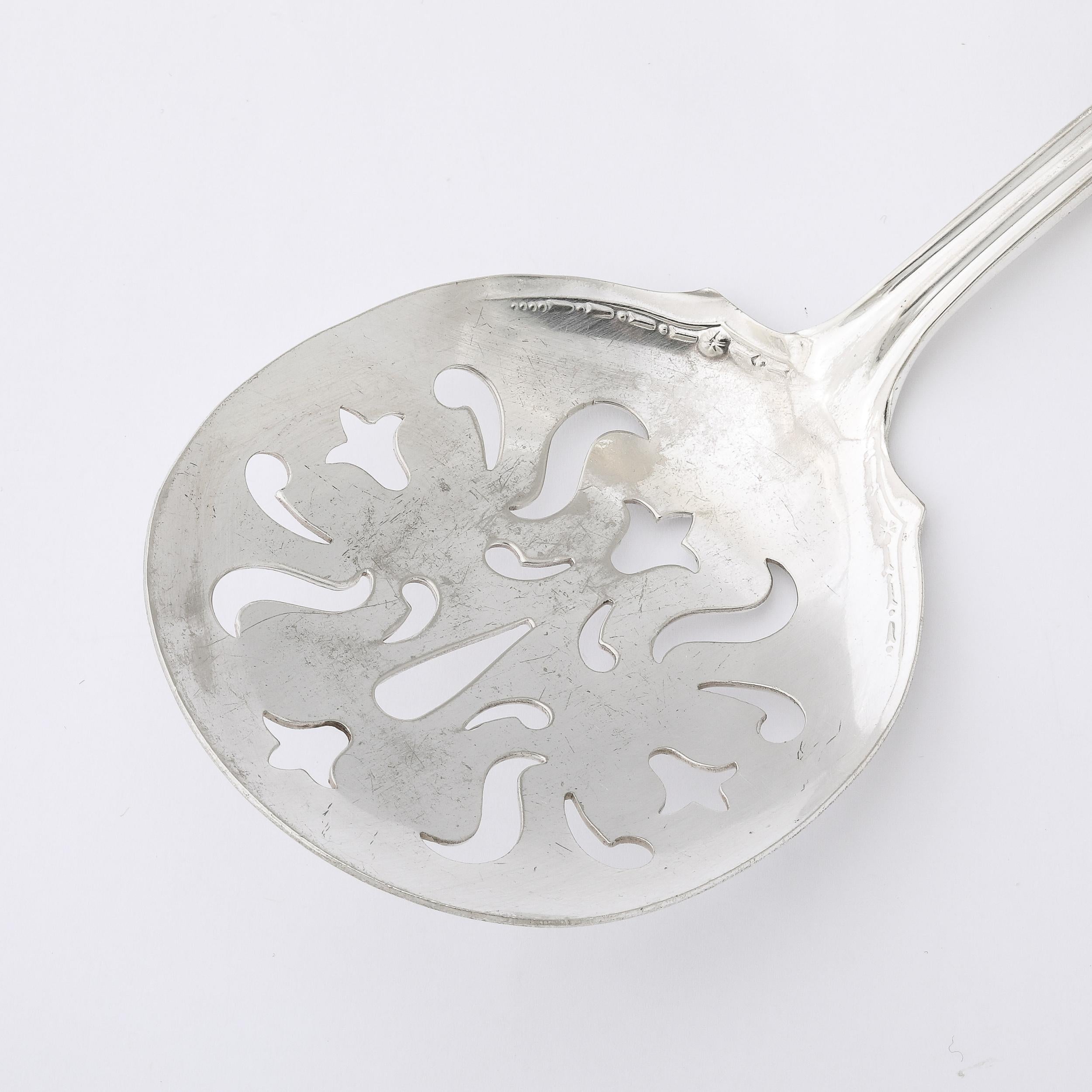 This gleaming and sophisticated Neoclassical Sterling Silver Pierced Serving Spoon W/Naturalist Relief Handle originates from the United States, Circa 1950. Features a lovely form of delicately balanced curves and excellent proportions, with serifed