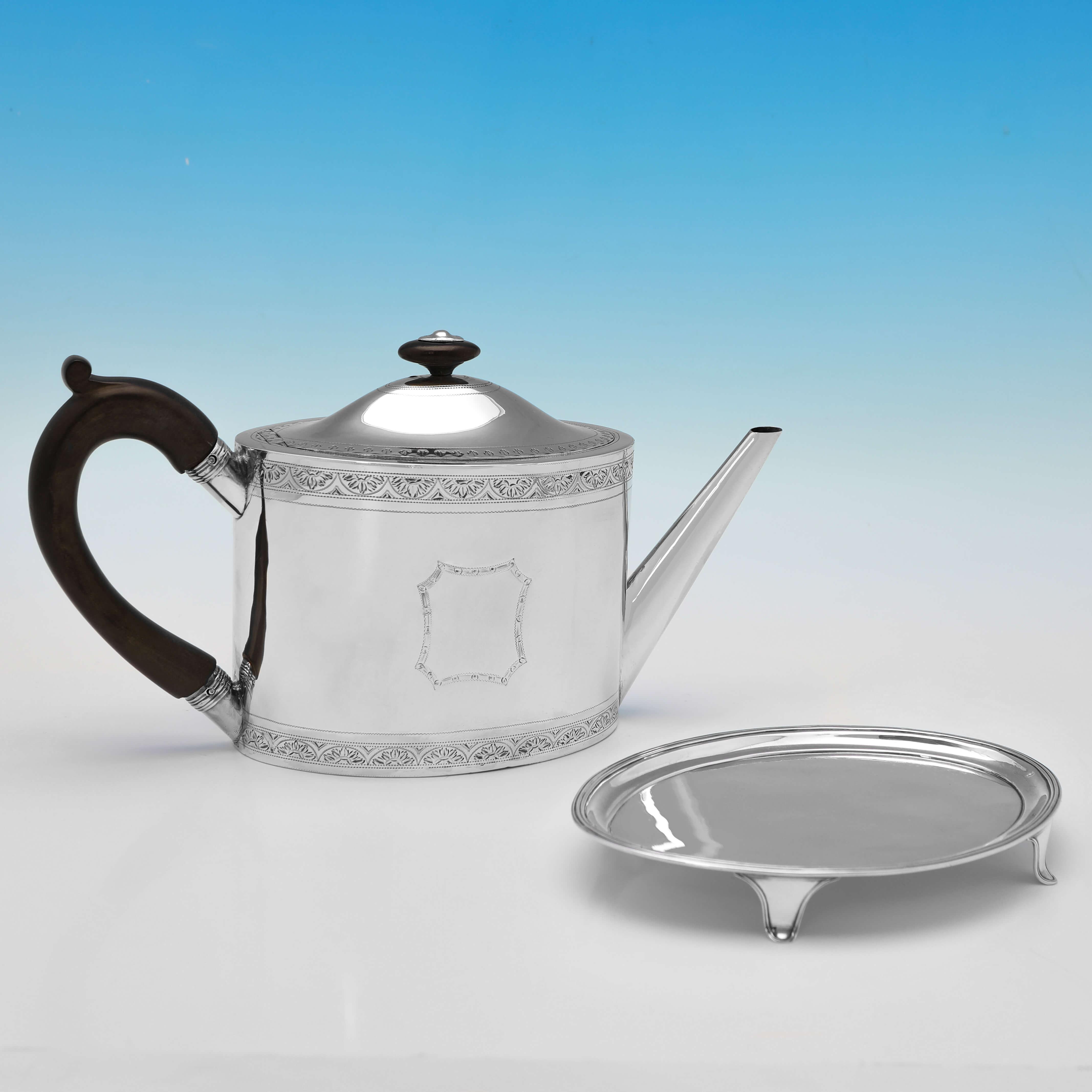 Hallmarked in London in 1793 by Henry Chawner, this handsome, George III, Antique Sterling Silver Teapot & Stand, is oval in shape, and features bright cut engraved decoration to the teapot, and a wooden handle and finial. 

The teapot on the stand