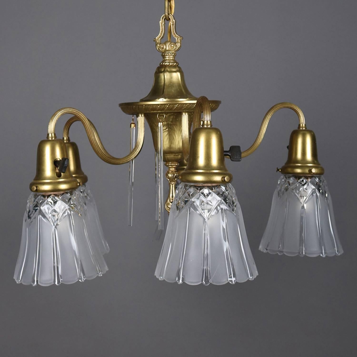 Neoclassical style gilt chandelier features gilt frame with urn form base decorated with cut crystal prisms and with five S-scroll arms terminating in drop lights with frosted pressed glass shades, signed Williamson on frame, newly re-wired, circa