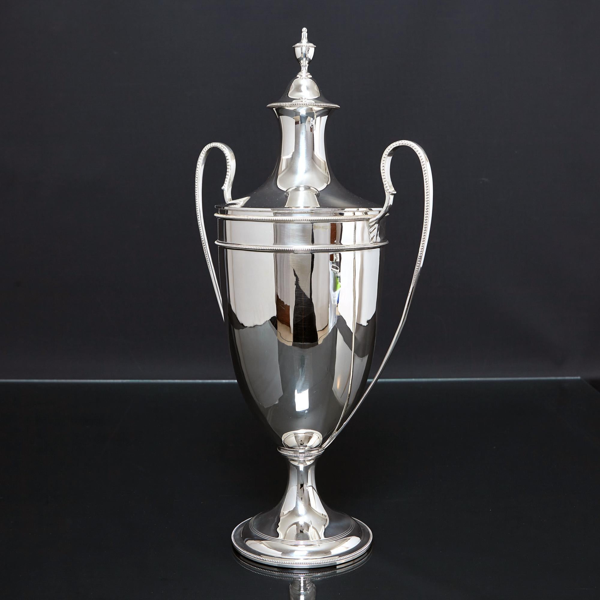 Elegant urn-shaped silver trophy cup and cover in the restrained and graceful neoclassical Adam style with long sweeping handles decorated with a fine bead decoration.  Two bands of bead decoration surround the body and the spreading silver base is